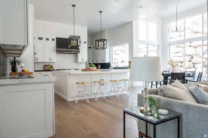 Open-concept kitchen featuring white cabinetry, a large center island with counter seating, wood-finish flooring, a black range hood, and a tiled backsplash