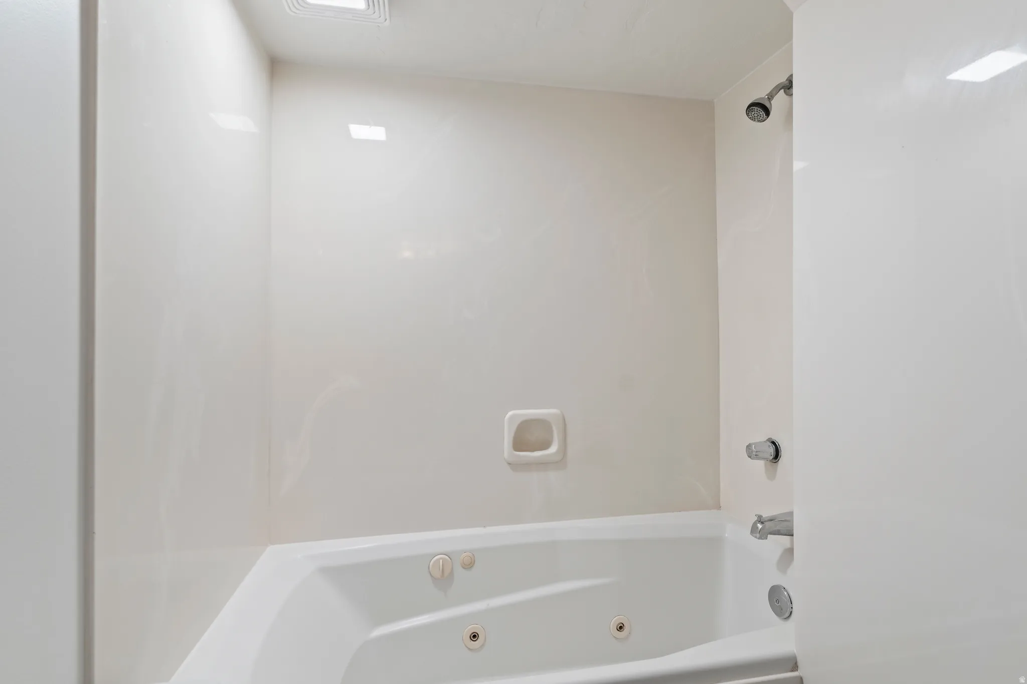 Bathtub and shower combination featuring an integrated corner jetted tub, a wall-mounted showerhead, and chrome fixtures