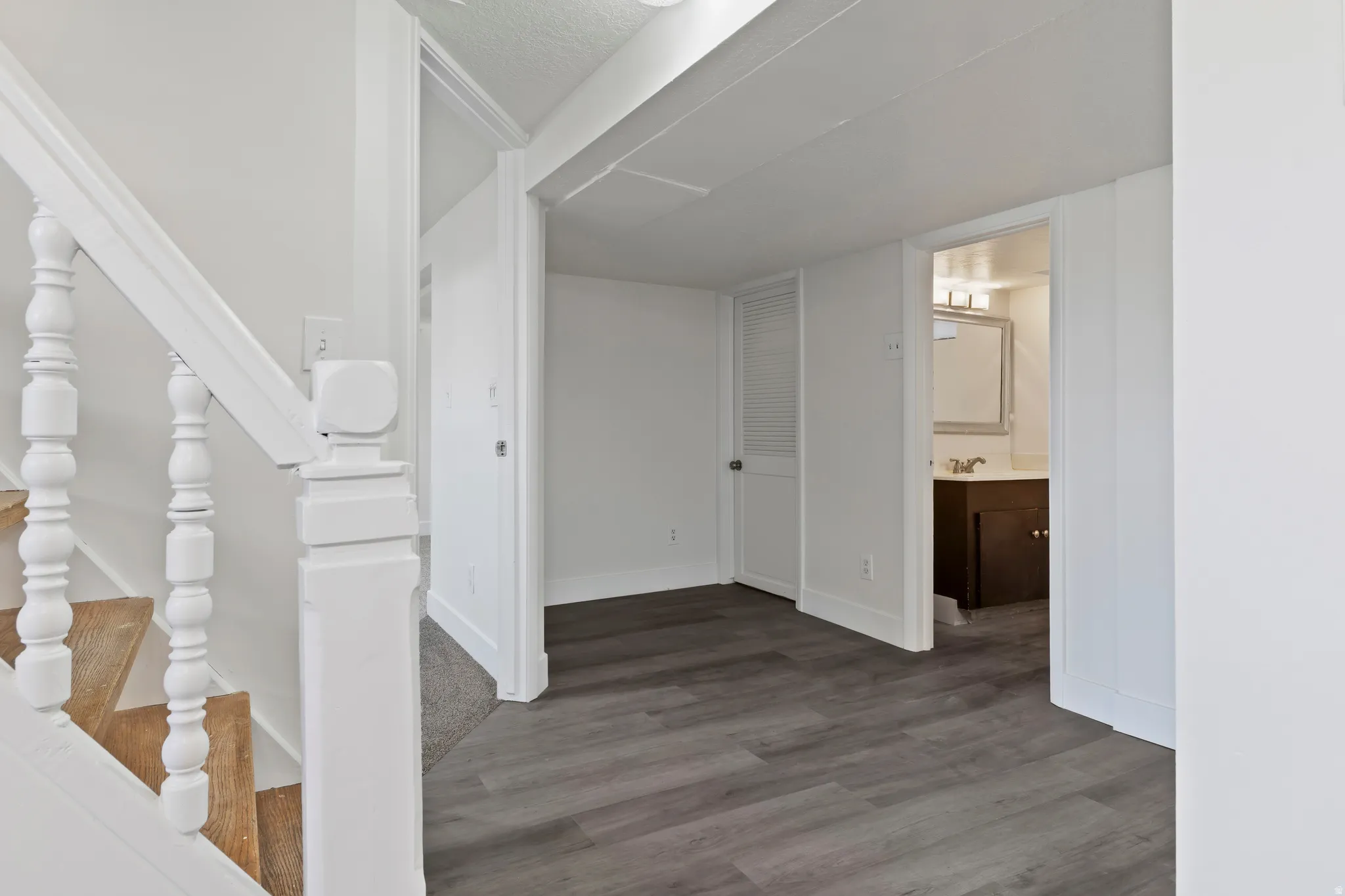 Interior hallway featuring wood-finish flooring, white trim, and a white staircase with turned balusters