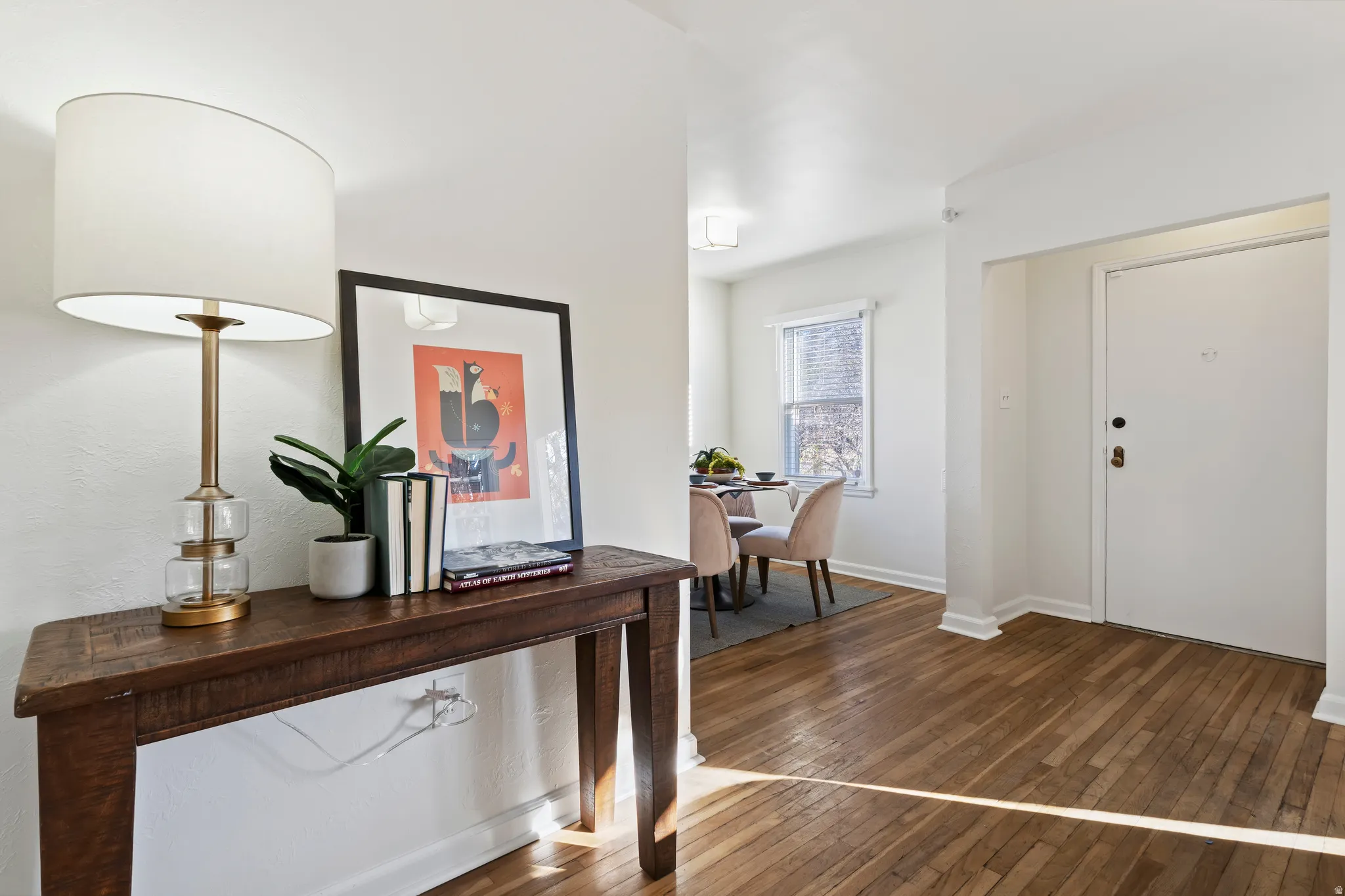Warm wood-finish flooring extends through the entry and into a dining area featuring a window with blinds