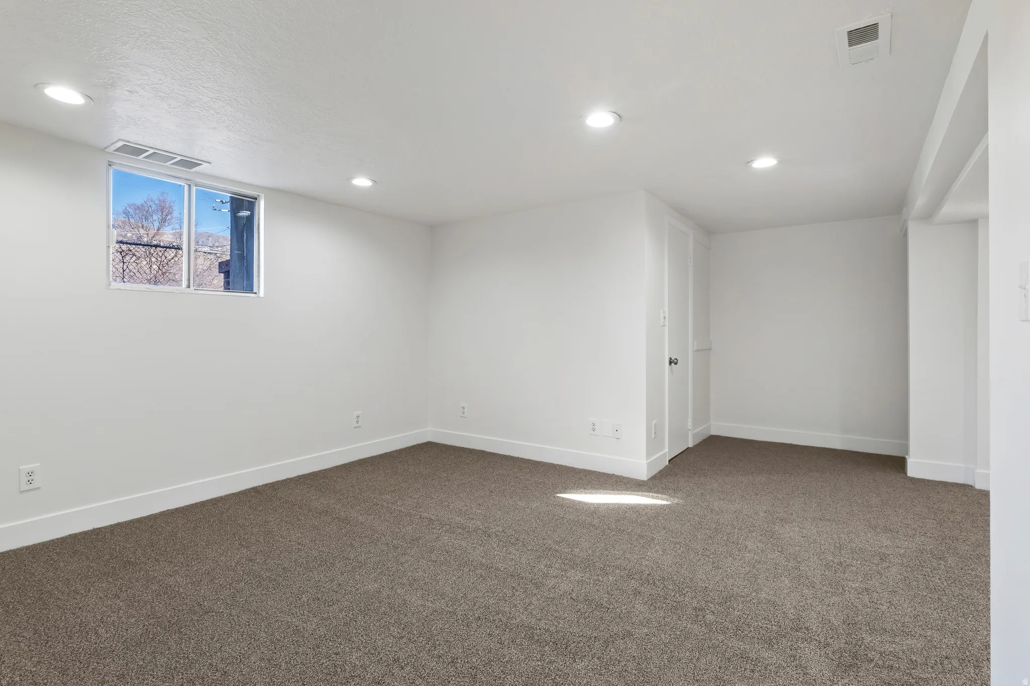 Spacious room featuring new carpeting, recessed lighting, a white trim package, and a window providing exterior visibility