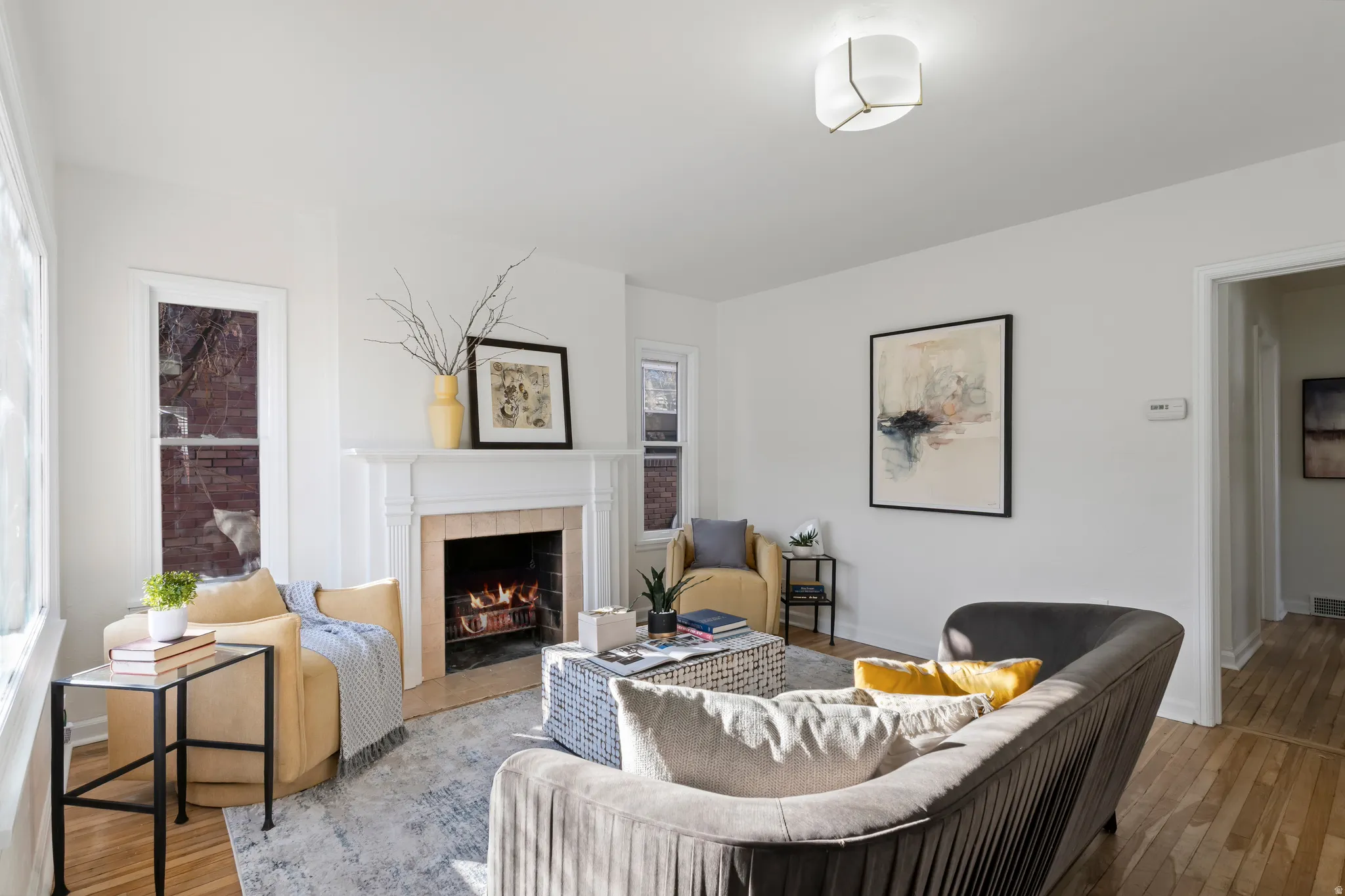 Living area featuring a classic white mantel fireplace with a light-colored tile surround, hardwood flooring, and abundant natural light from multiple windows