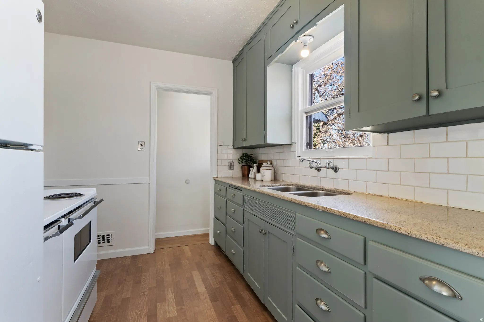 Kitchen featuring a double basin sink, light-toned countertops, subway tile backsplash, and light green cabinetry