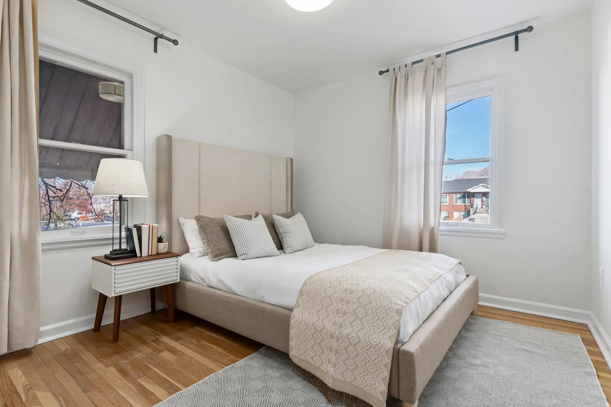 Bedroom featuring wood-finish flooring, white walls, and two windows with black curtain rods