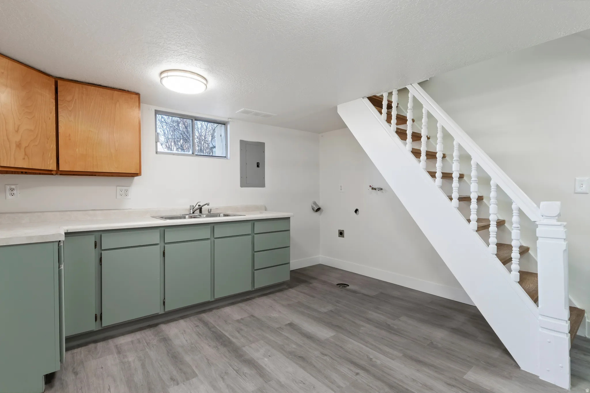 Utility area featuring wood-finish flooring, a white spindle staircase, and a counter space with an integrated sink