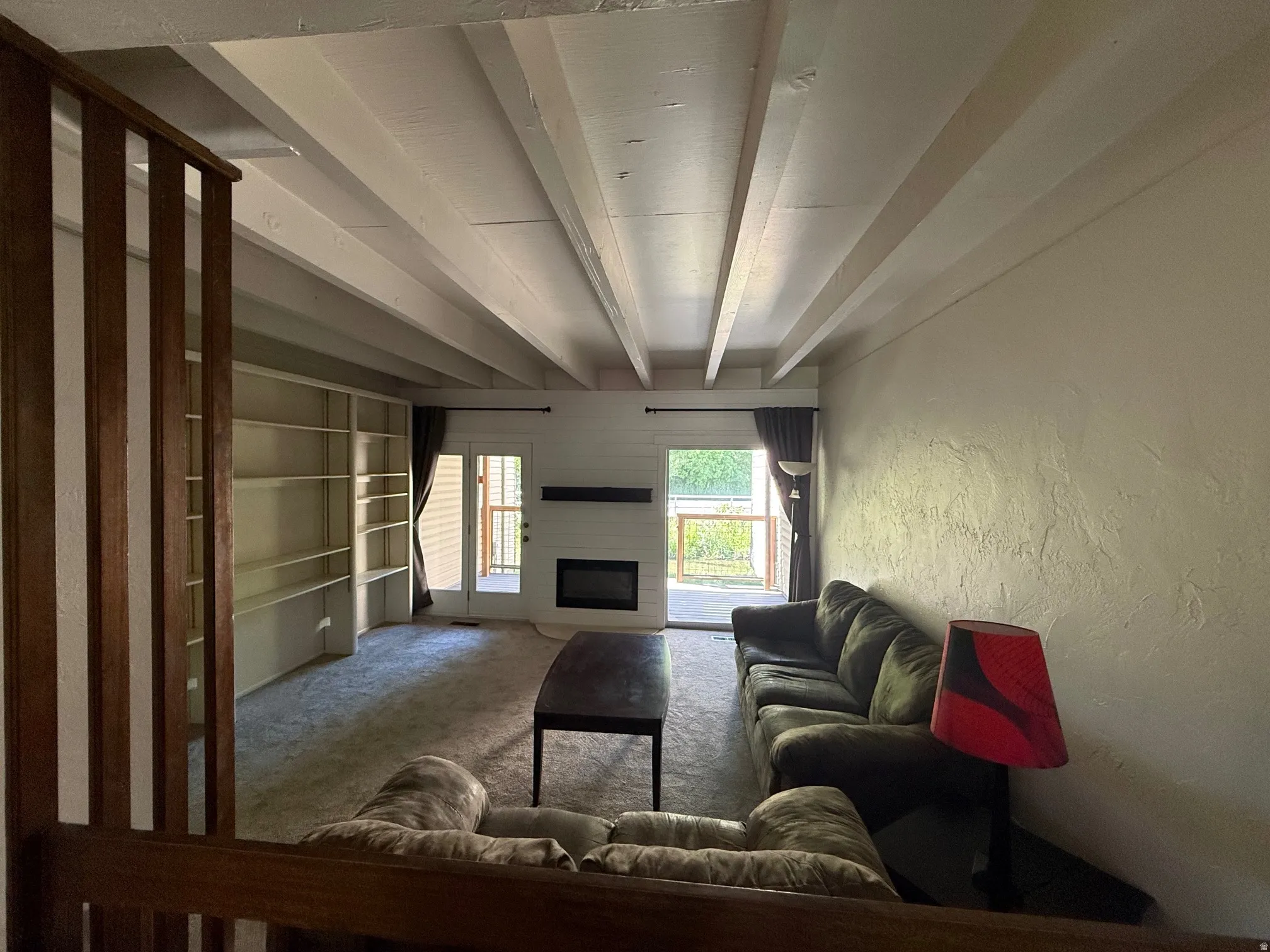 Living area featuring exposed beam ceiling, built-in shelving, an electric fireplace and deck access.