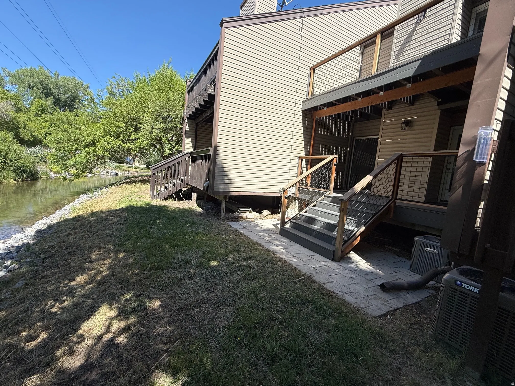 Waterside exterior featuring light-toned siding, a multi-level deck system with wood railing with wire infill, and a lower-level paver patio
