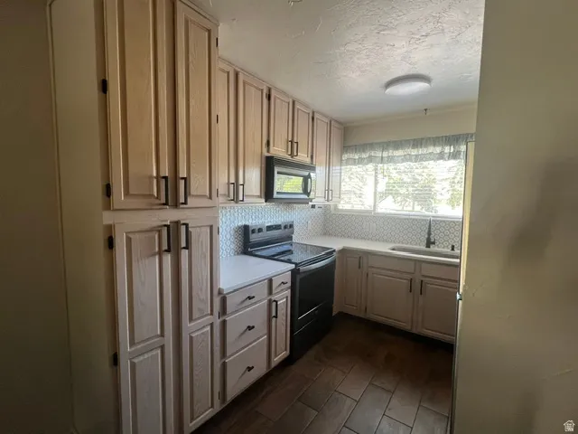 Kitchen featuring extensive light wood-finish cabinetry, new quartz countertops, decorative tile backsplash, built-in microwave and smooth top range.