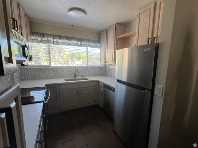 Bright kitchen featuring light wood-finish cabinetry, stainless steel appliances, a patterned tile backsplash, and wood-look tile flooring