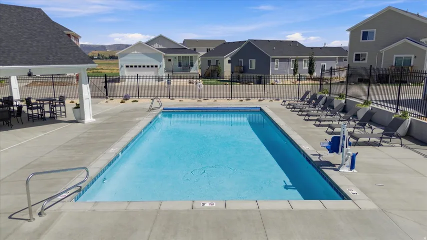 Outdoor swimming pool with concrete surround, wrought iron style fencing, and an adjacent shaded pergola
