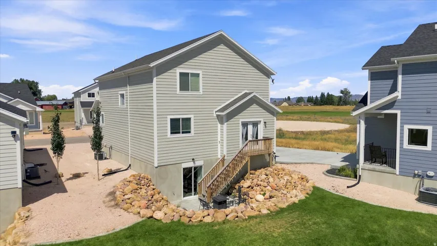 Rear exterior featuring a walk-out basement, upper-level deck, gravel hardscaping with rock accents, and manicured shared green space