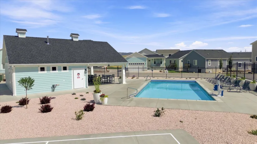 Community swimming pool with concrete decking, surrounding black metal fencing, and an adjacent structure featuring light blue siding