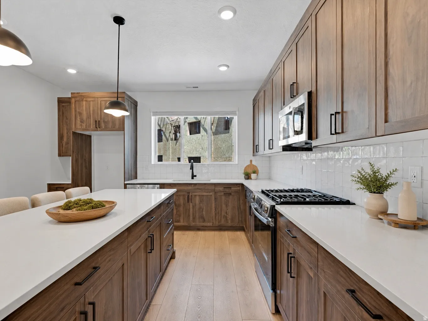 Modern kitchen featuring an expansive center island with seating, wood-finish cabinetry, stainless steel appliances, and light countertops