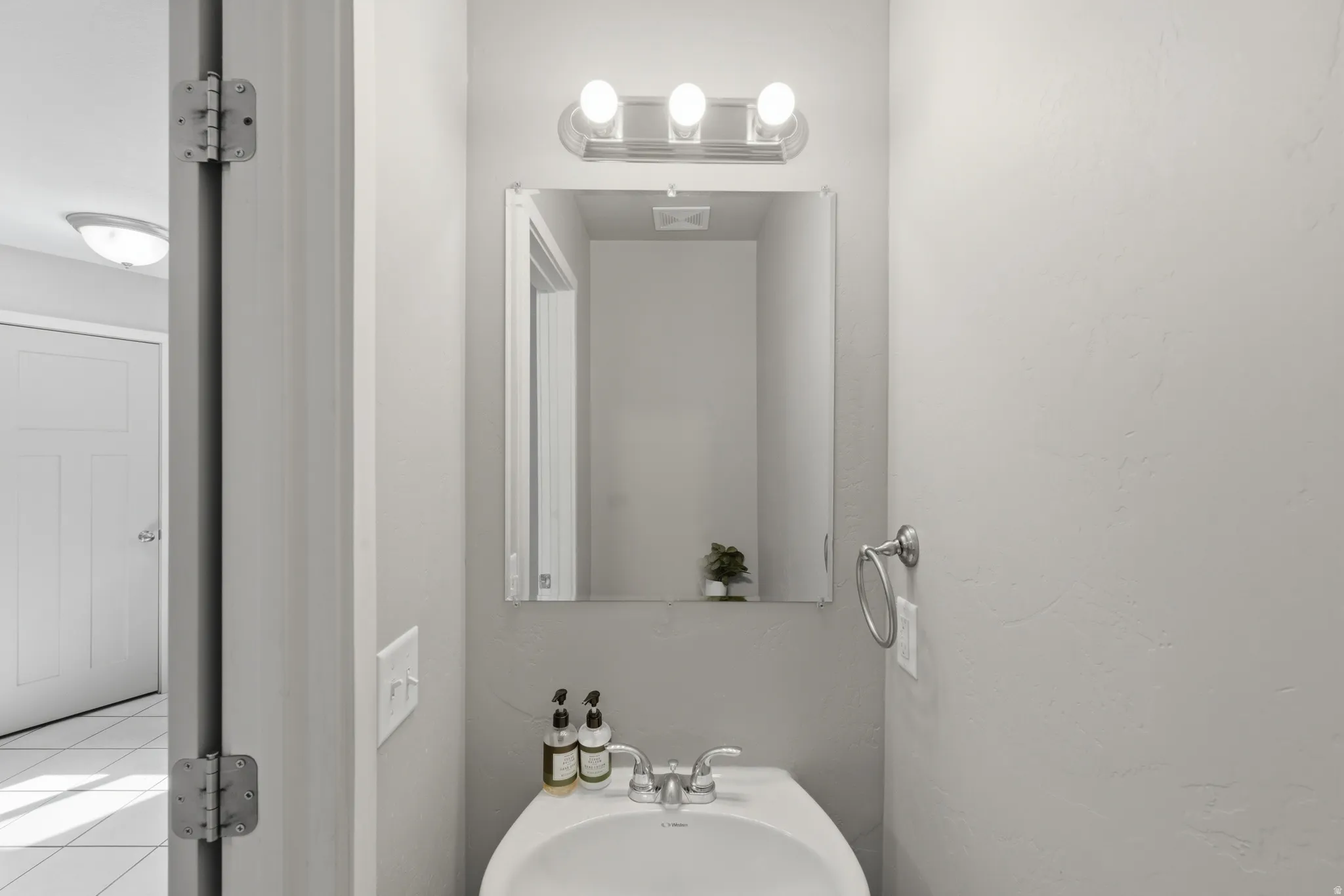 Bathroom vanity featuring a white ceramic sink, wall-mounted faucet, and a rectangular mirror with a three-bulb light fixture above