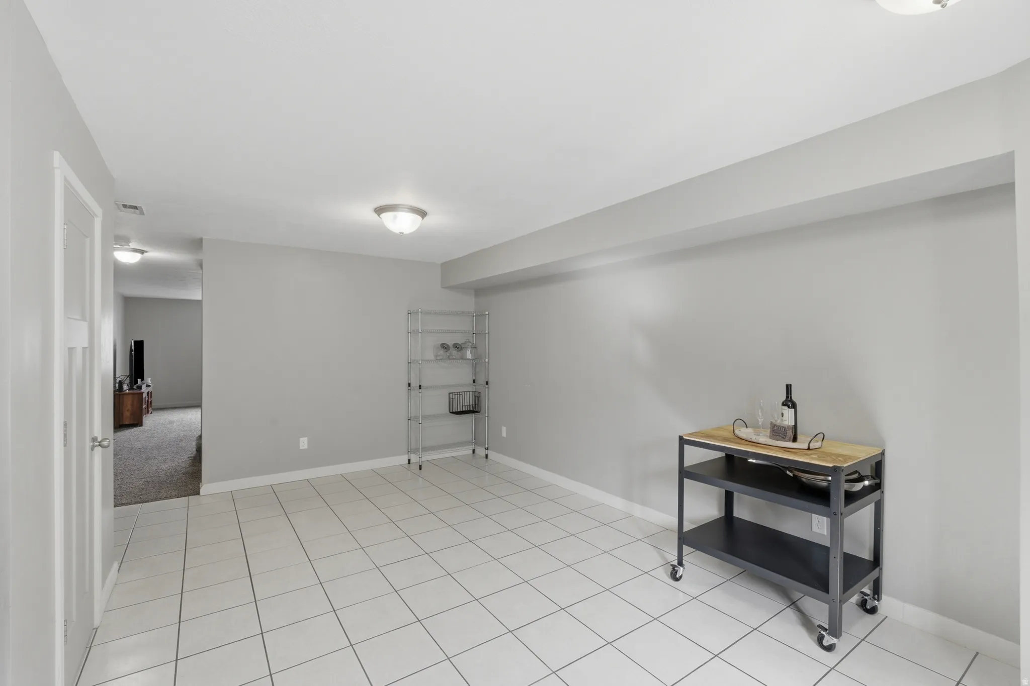 Spacious room featuring light-toned tile flooring, neutral wall paint, and ceiling-mounted lighting fixtures