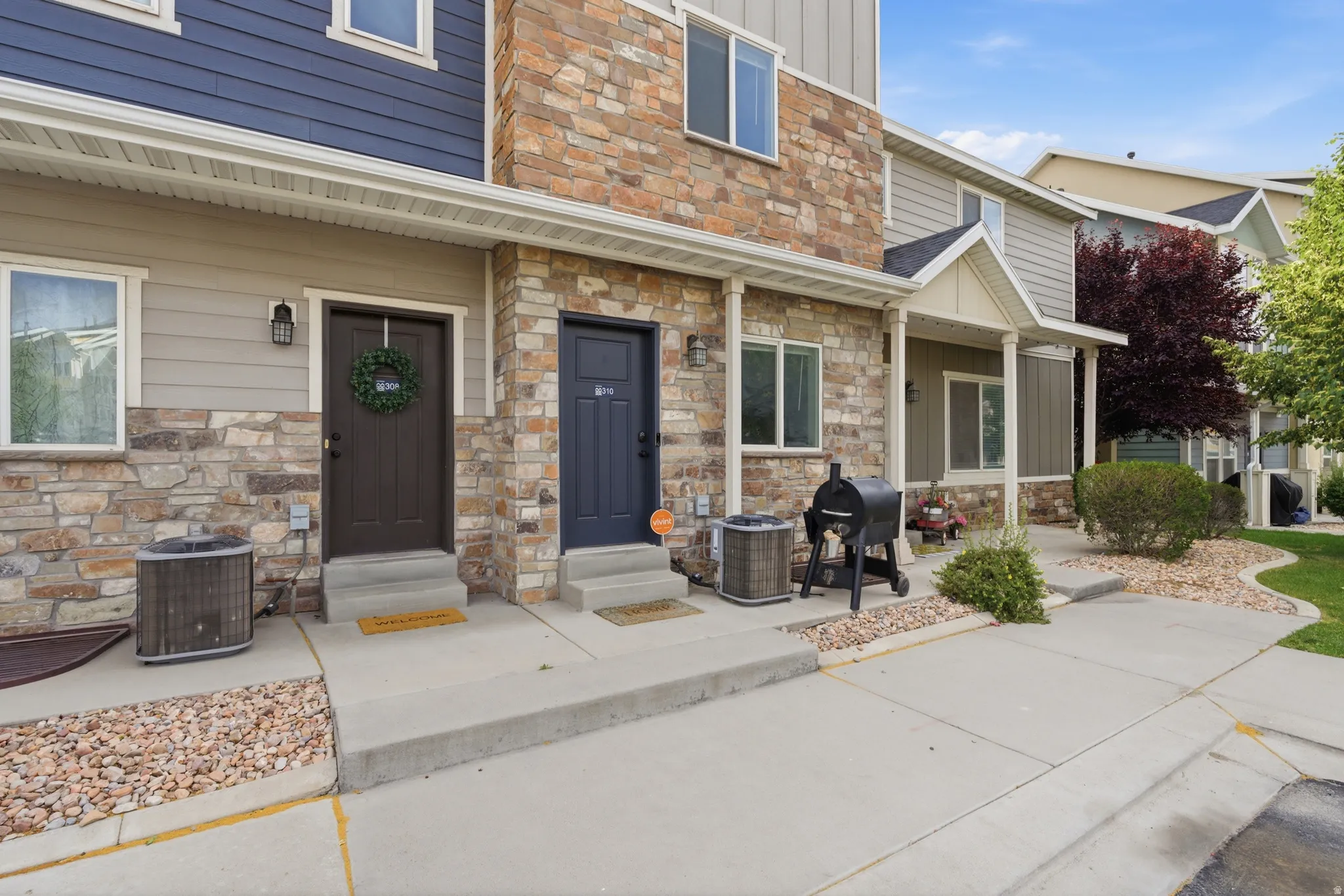 Exterior featuring stone veneer and horizontal siding, with multiple entryways, paved walkways, and landscaped rock beds