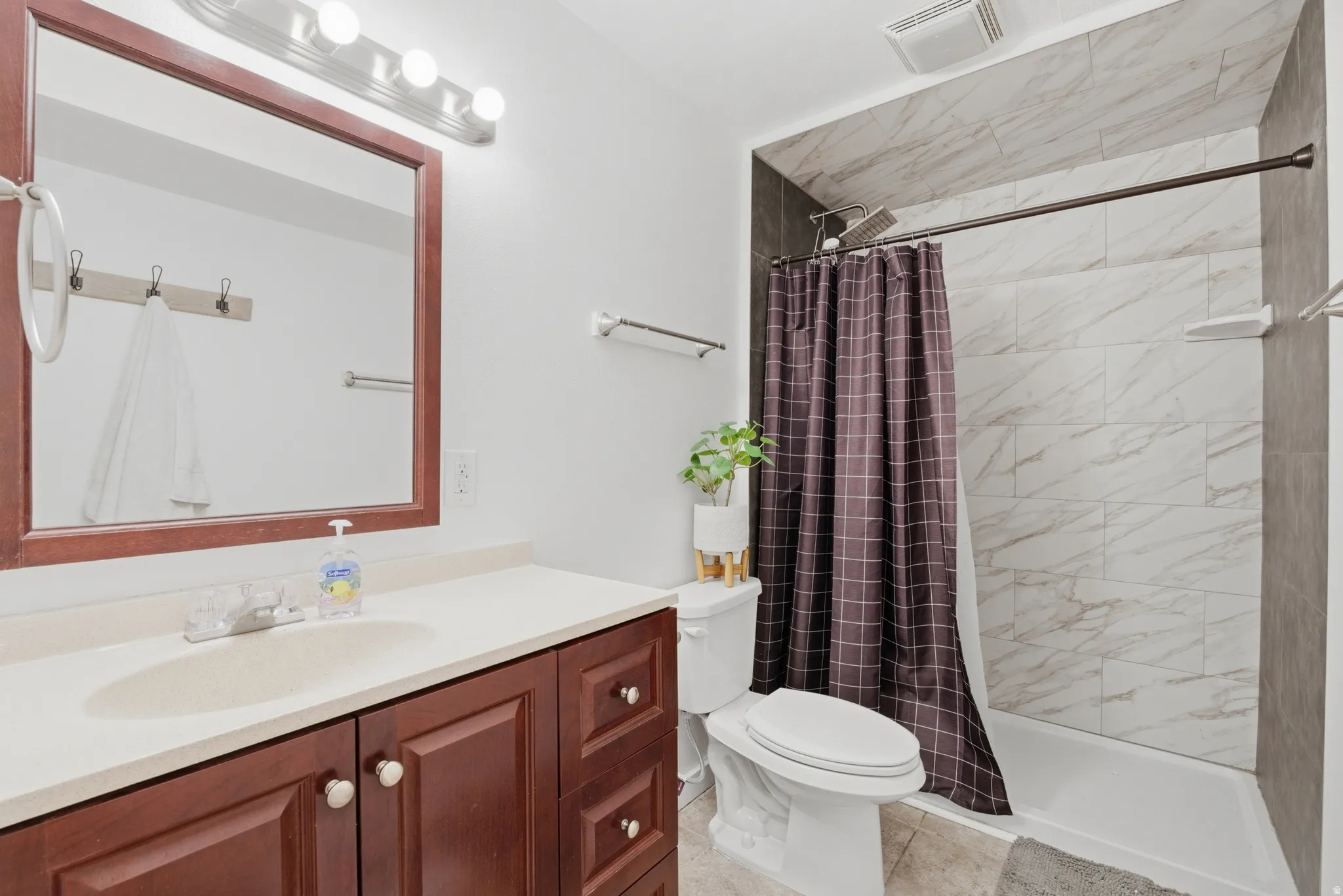Bathroom featuring a white ceramic toilet, a combination shower and tub with marble-look tile surround, and a wood-finish vanity with a light-colored countertop
