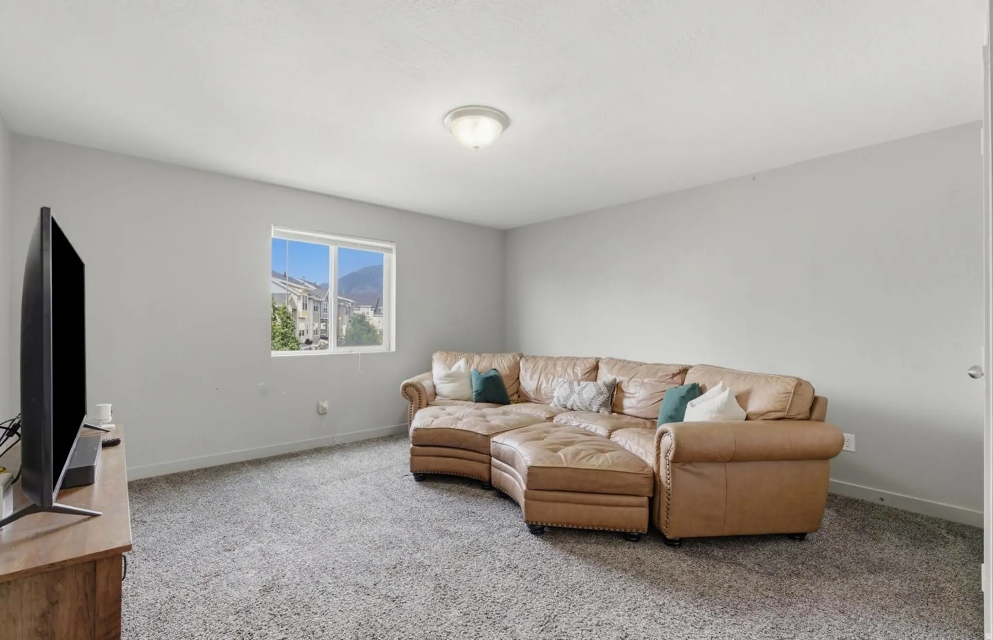 Carpeted recreation room featuring neutral painted walls, a flush-mount ceiling light, and a white-framed window
