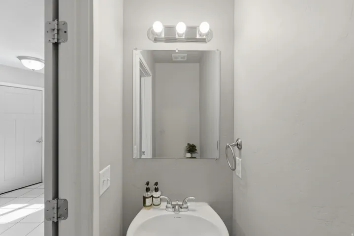Bathroom vanity featuring a white ceramic sink, wall-mounted faucet, and a rectangular mirror with a three-bulb light fixture above