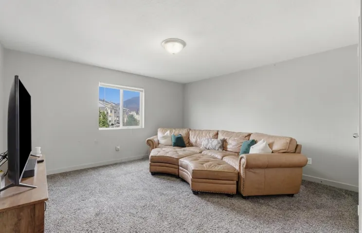 Carpeted recreation room featuring neutral painted walls, a flush-mount ceiling light, and a white-framed window