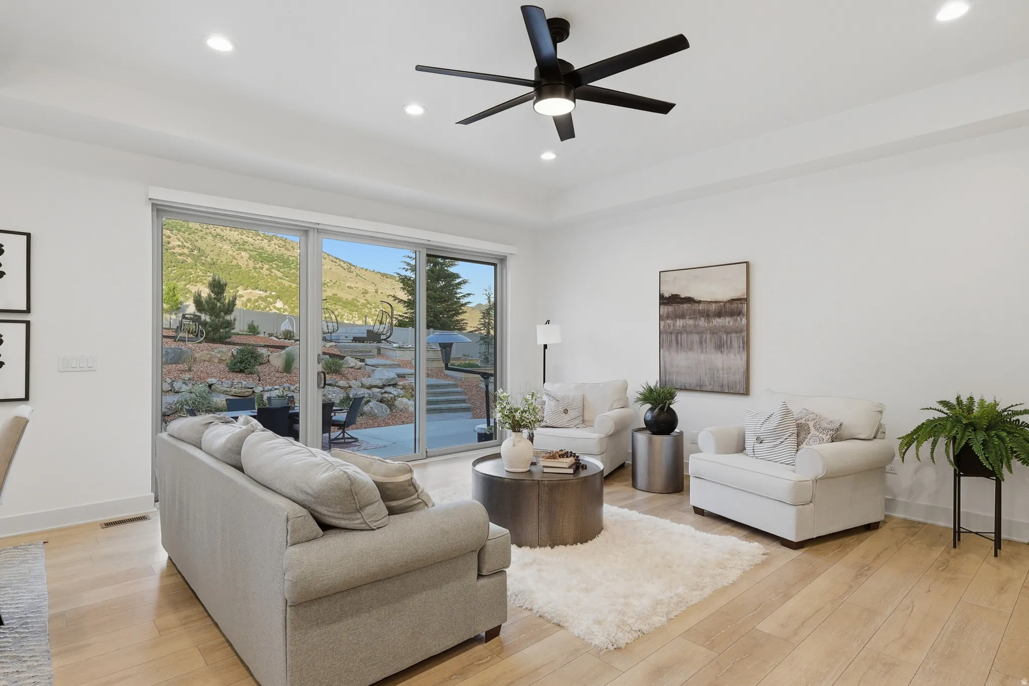 Spacious living area featuring light wood-finish flooring, a contemporary ceiling fan with integrated lighting, and recessed lighting