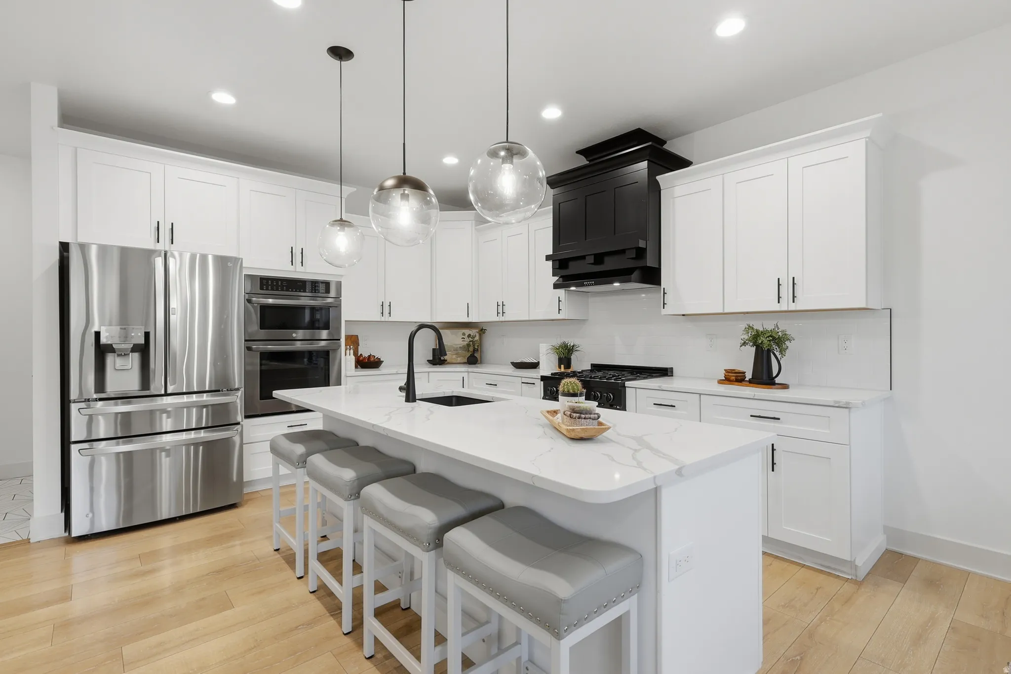 Contemporary kitchen featuring a large central island with seating, white shaker-style cabinetry, and stainless steel appliances