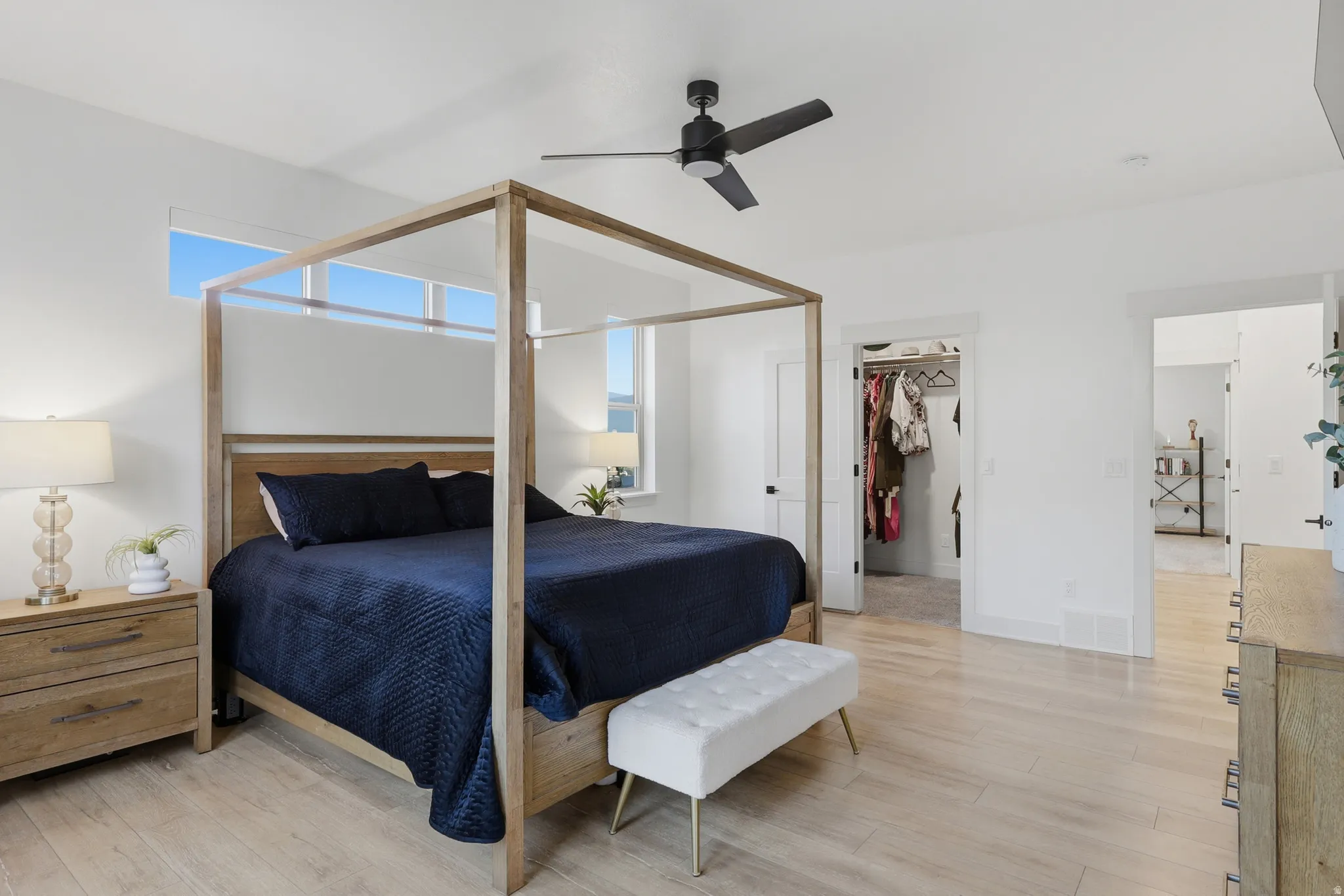 Spacious bedroom featuring light wood-finish flooring, a ceiling fan, transom windows, and a walk-in closet
