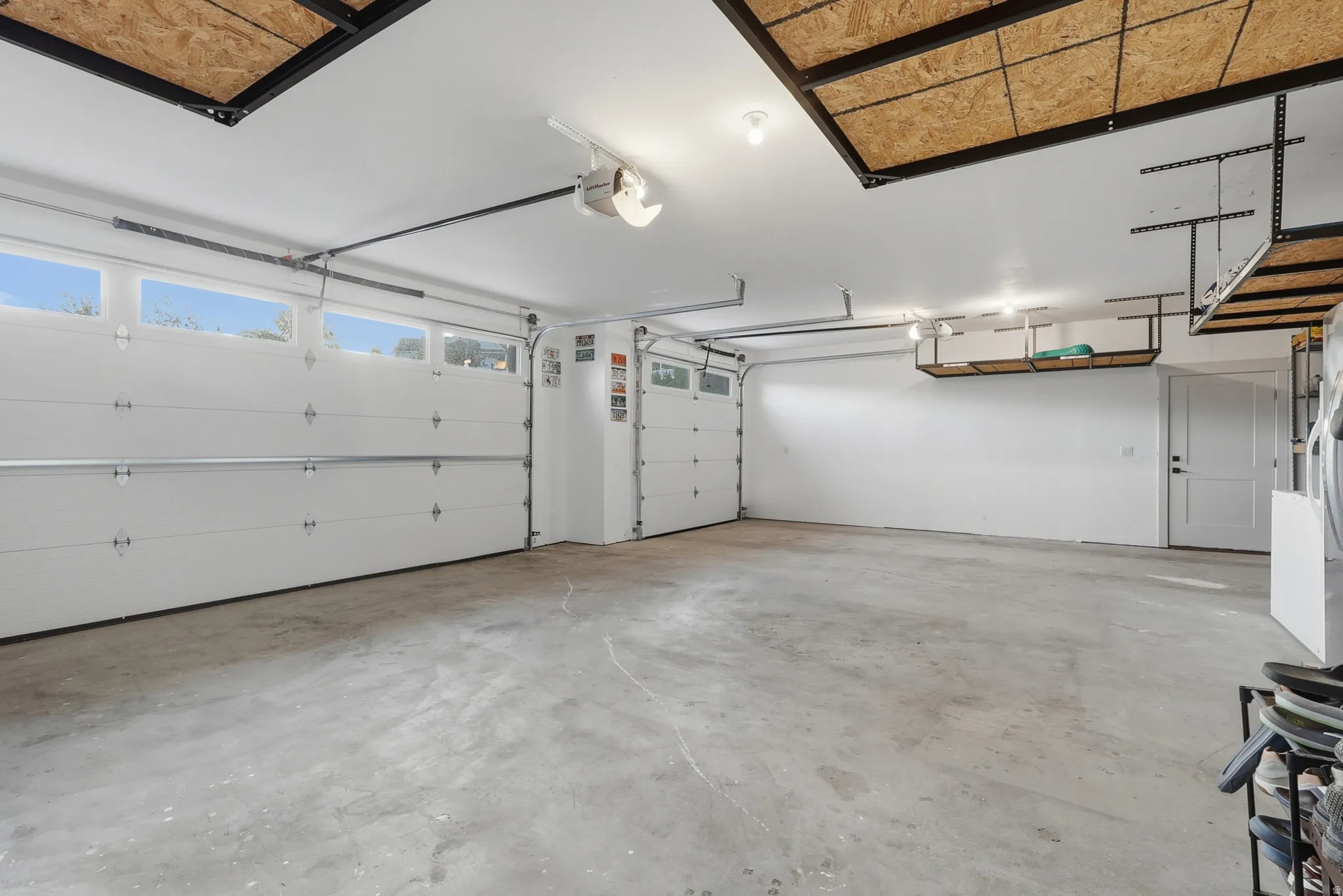 Spacious garage featuring two overhead doors with transom windows, a concrete floor, and ample overhead storage shelving
