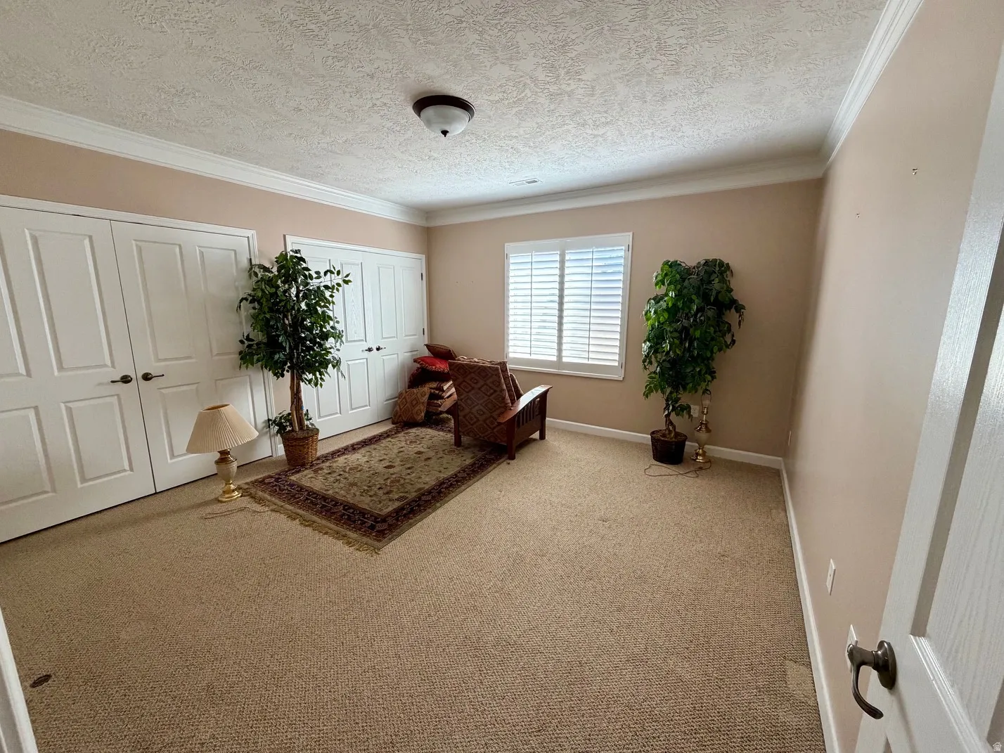 Carpeted room with a ceiling-mounted light fixture, crown molding, and two sets of bi-fold closet doors
