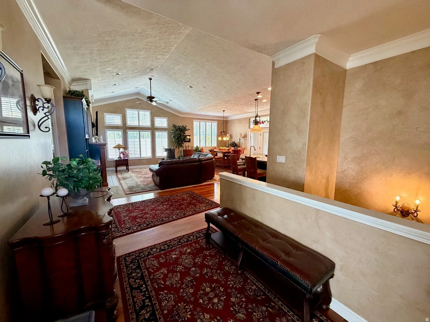 Vaulted ceiling with a central fan, hardwood flooring, and extensive window array with plantation shutters
