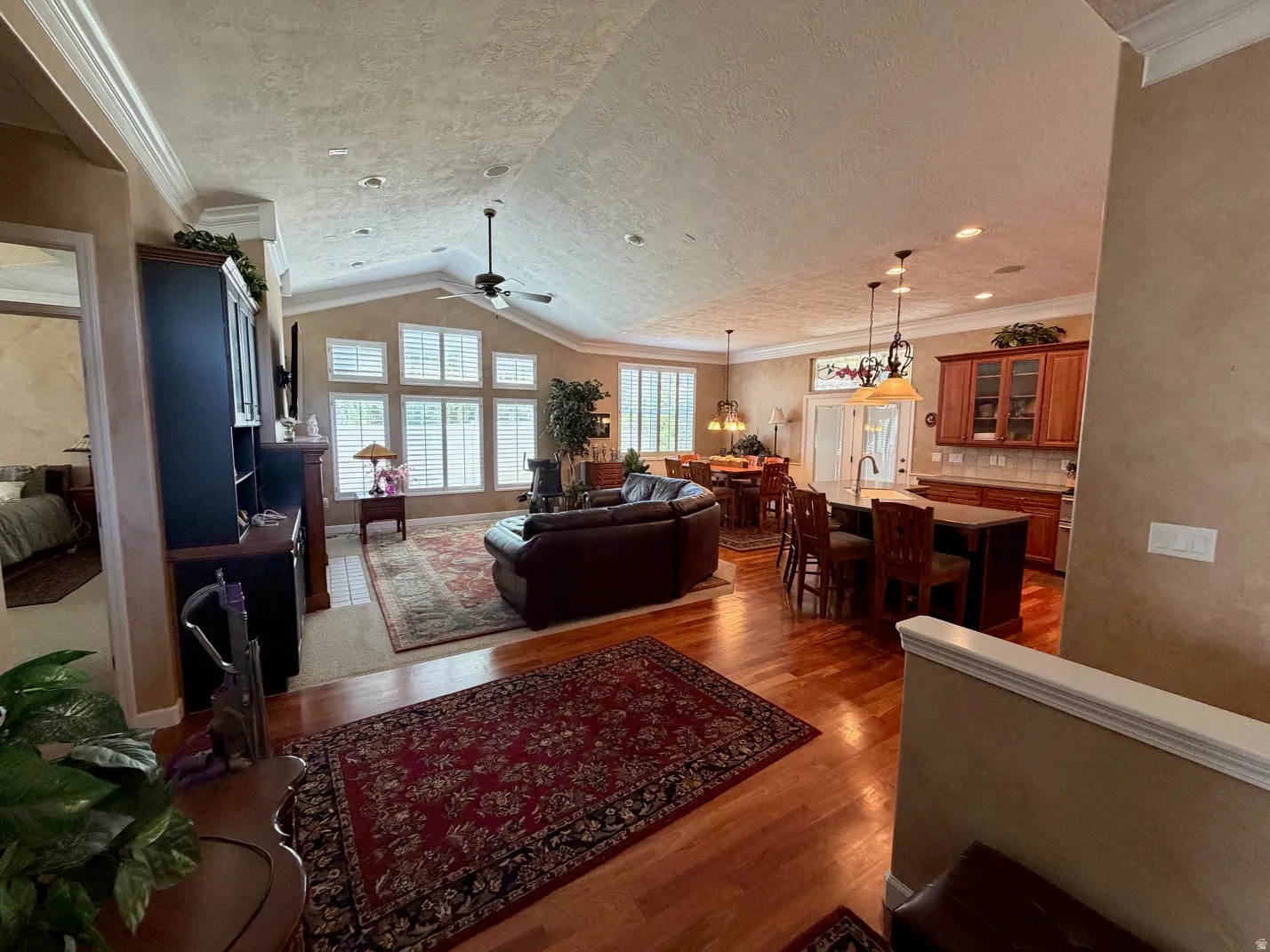 Open-concept living area featuring wood-finish flooring, vaulted ceilings, and extensive window treatments