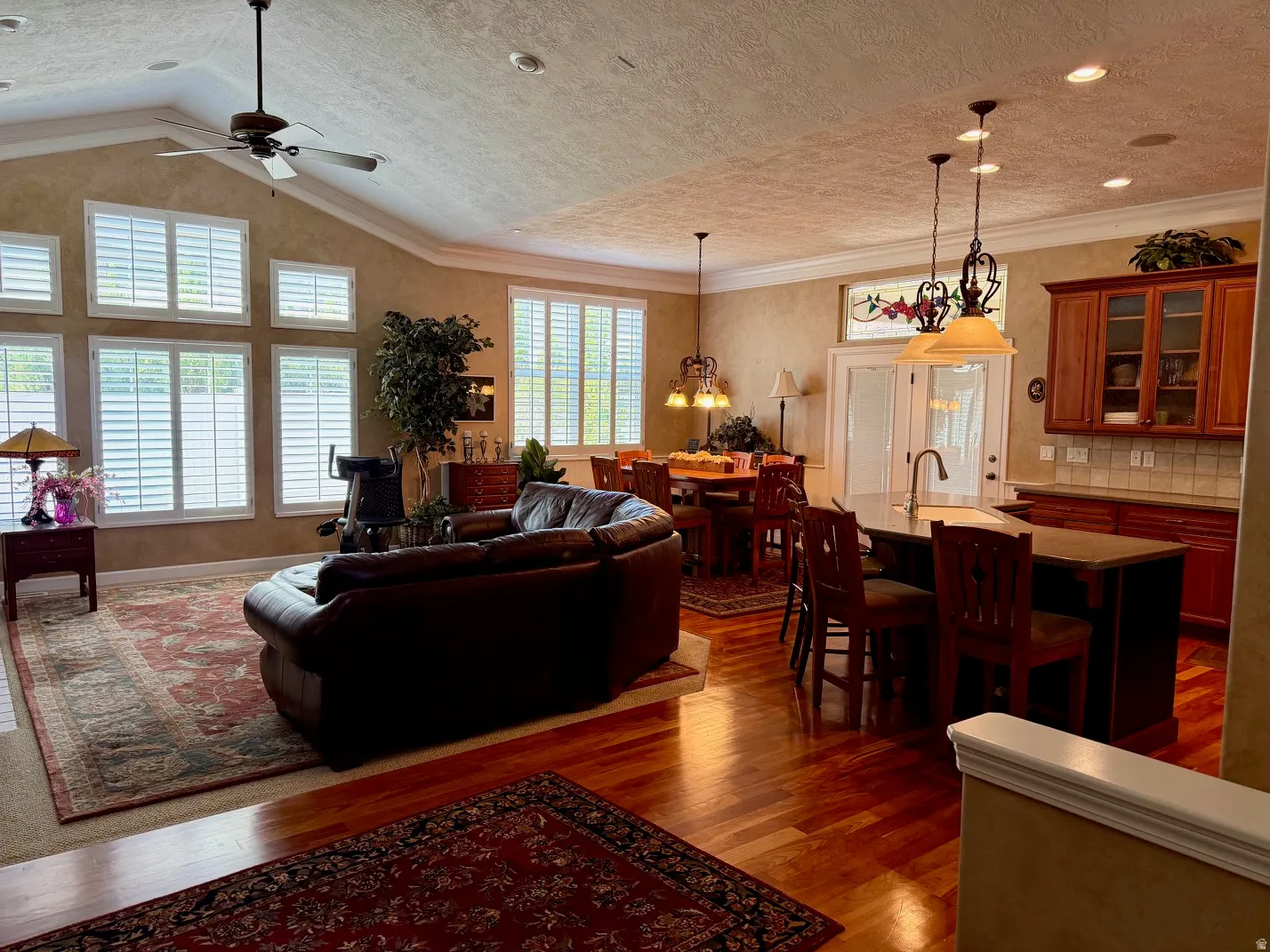 Open-concept living space featuring wood-finish flooring, vaulted ceilings, and extensive window treatments