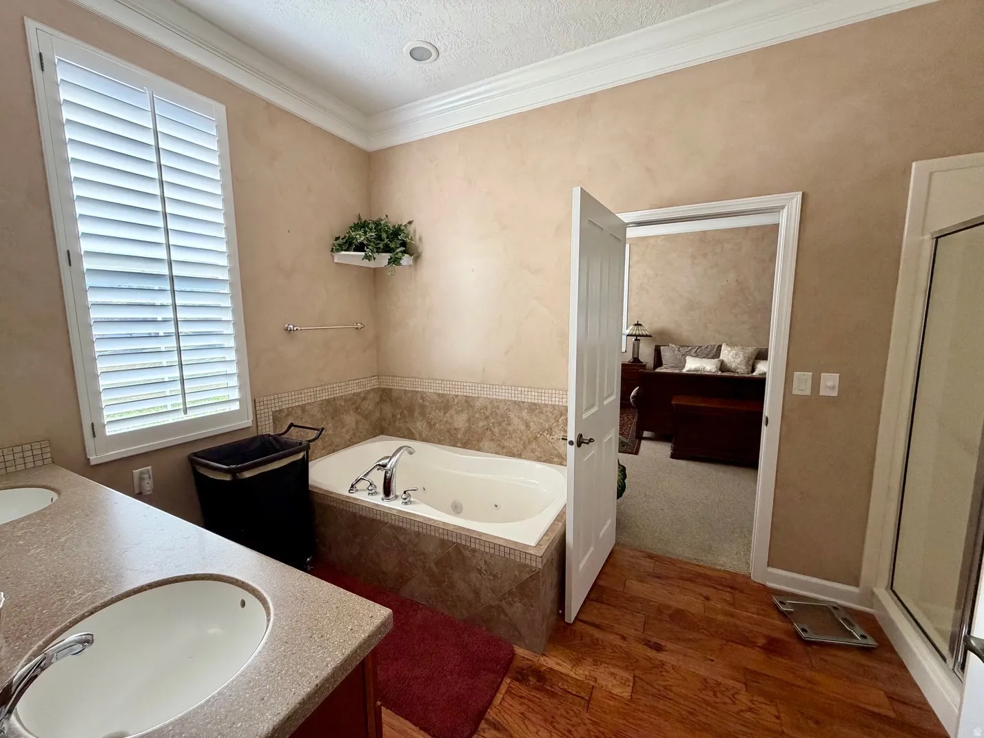 Bathroom featuring a jetted soaking tub with tile surround, a dual vanity with undermount sinks and light-toned countertops, and wood-finish flooring