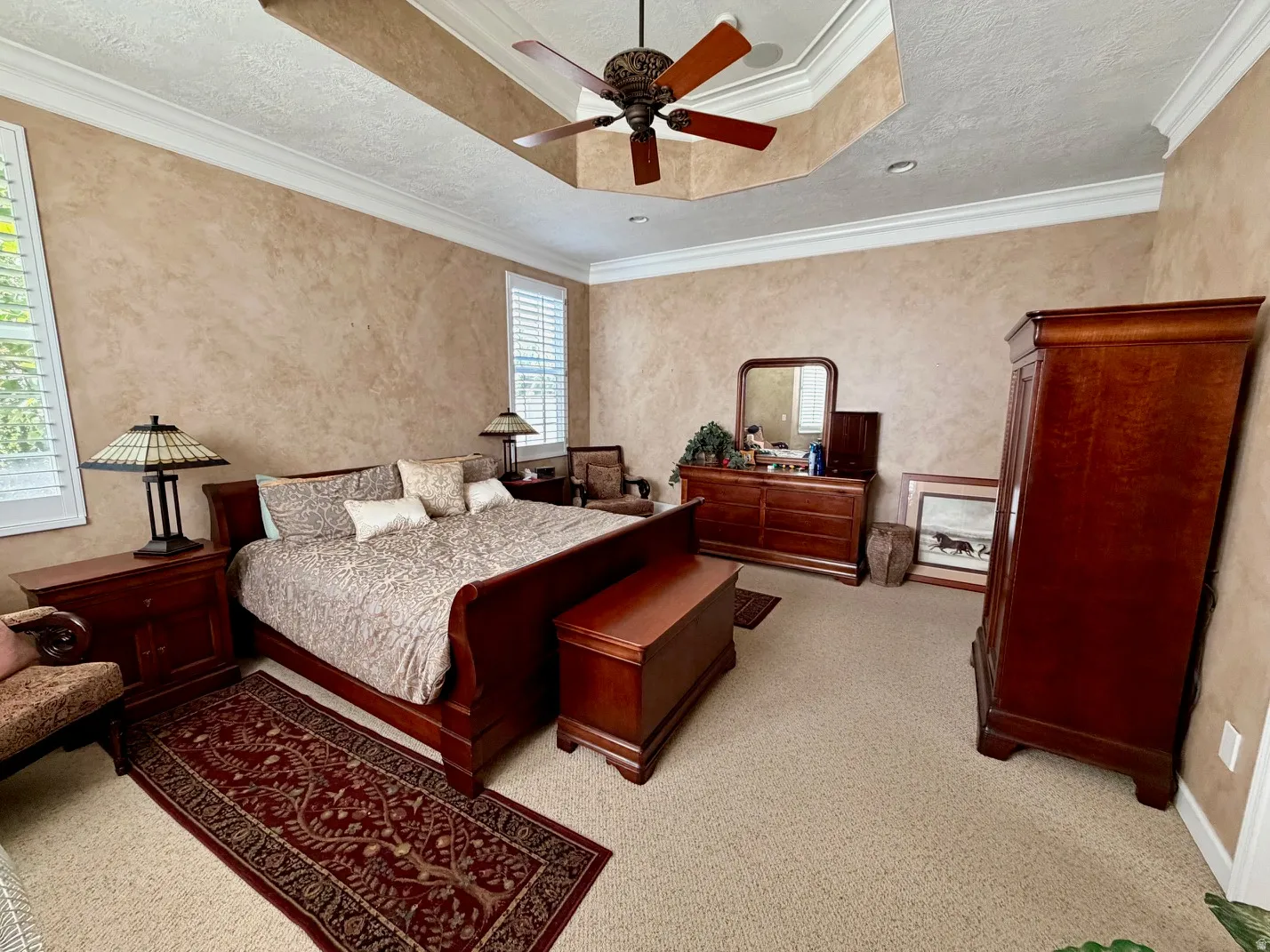 Spacious room featuring textured walls, crown molding, a tray ceiling with a built-in ceiling fan, and white plantation shutters