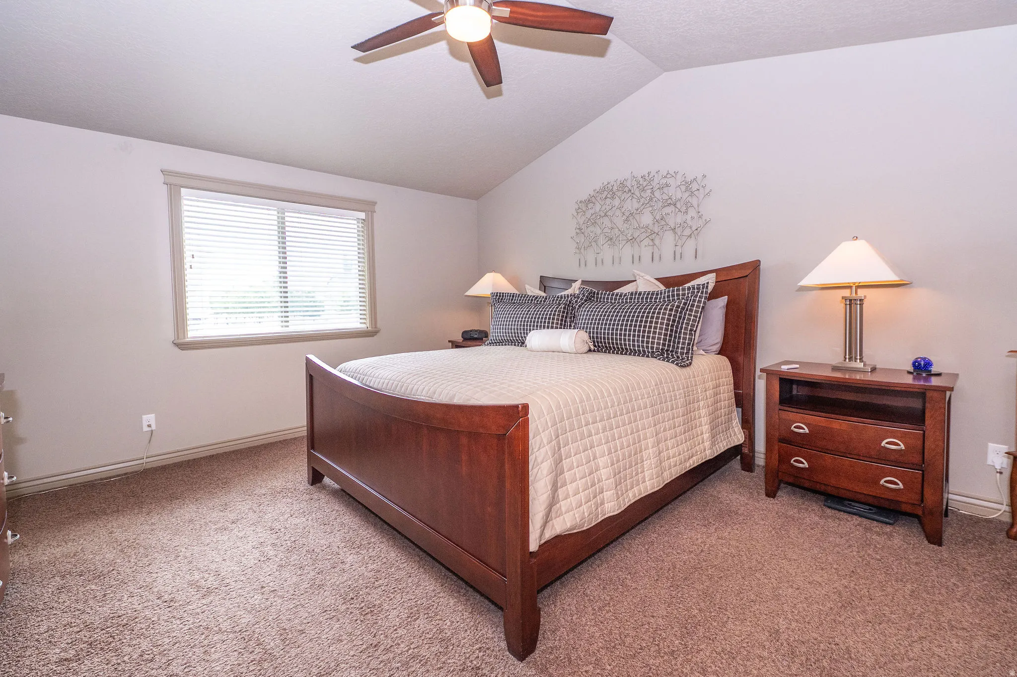 Carpeted room featuring a vaulted ceiling and a wood-finish ceiling fan with integrated lighting