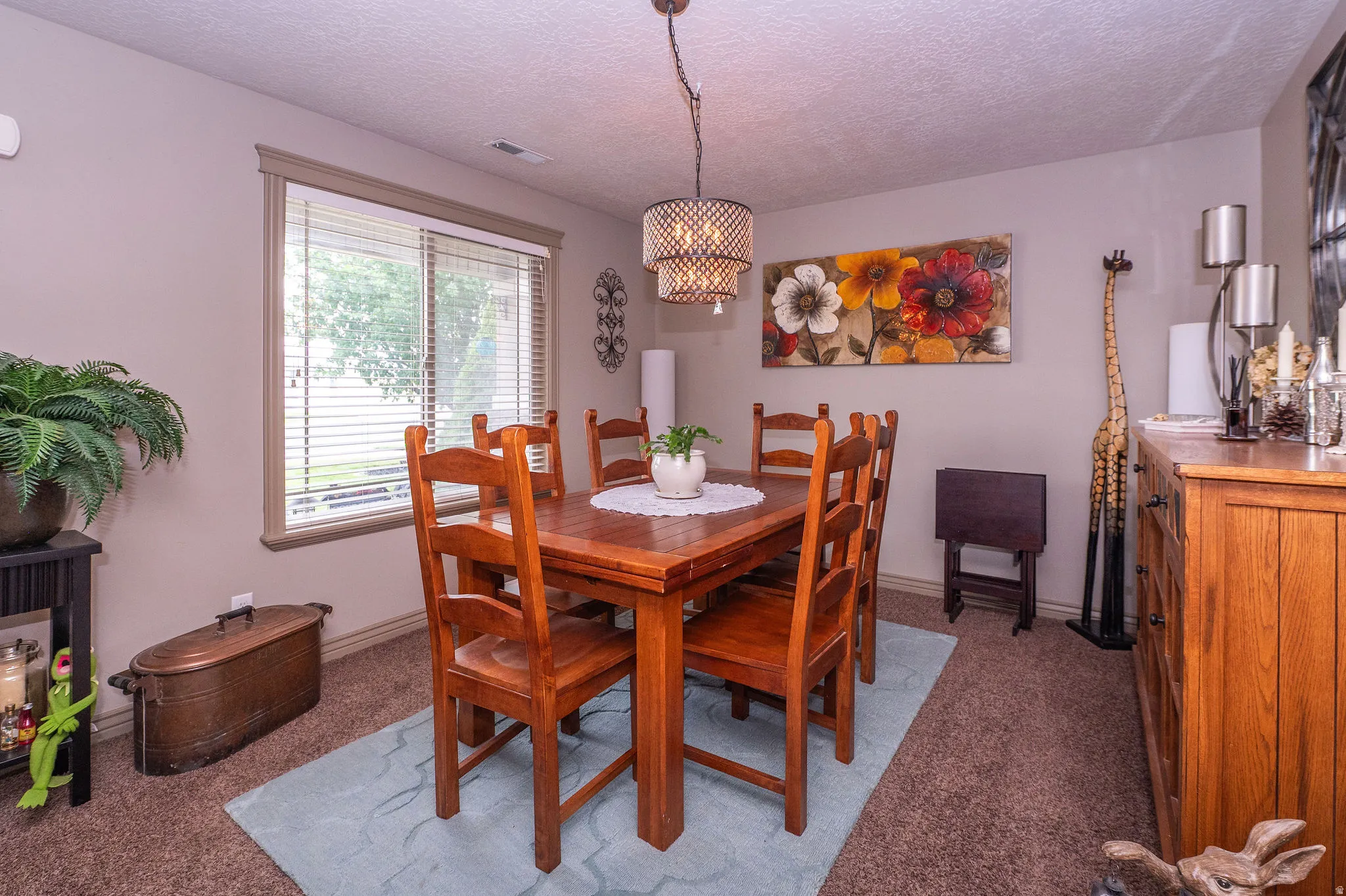 Carpeted dining area with a multi-light chandelier, a single window featuring blinds, and a built-in wood-finish buffet