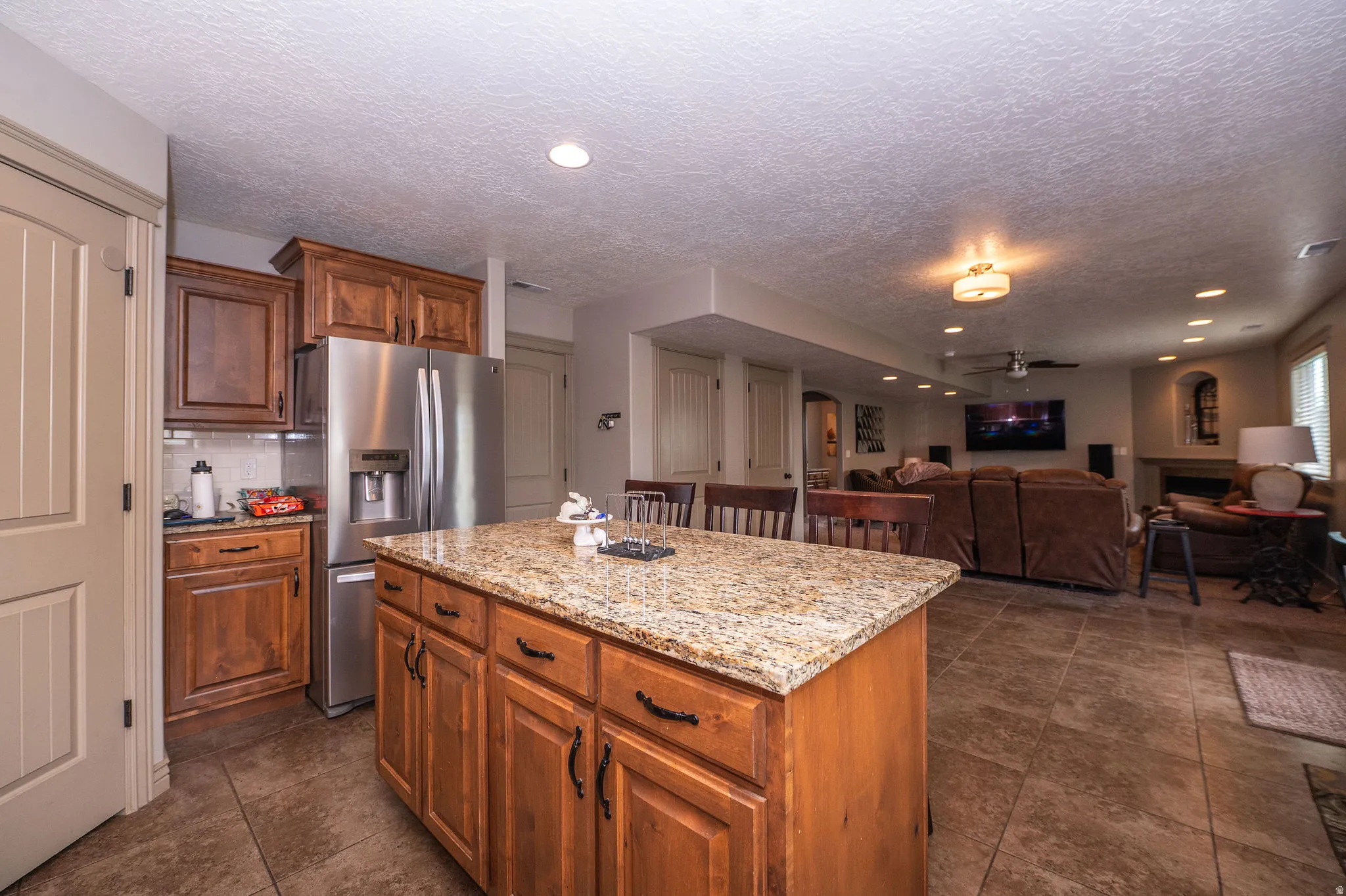 Kitchen island with granite countertop and rich wood cabinetry, stainless steel refrigerator, and tiled flooring