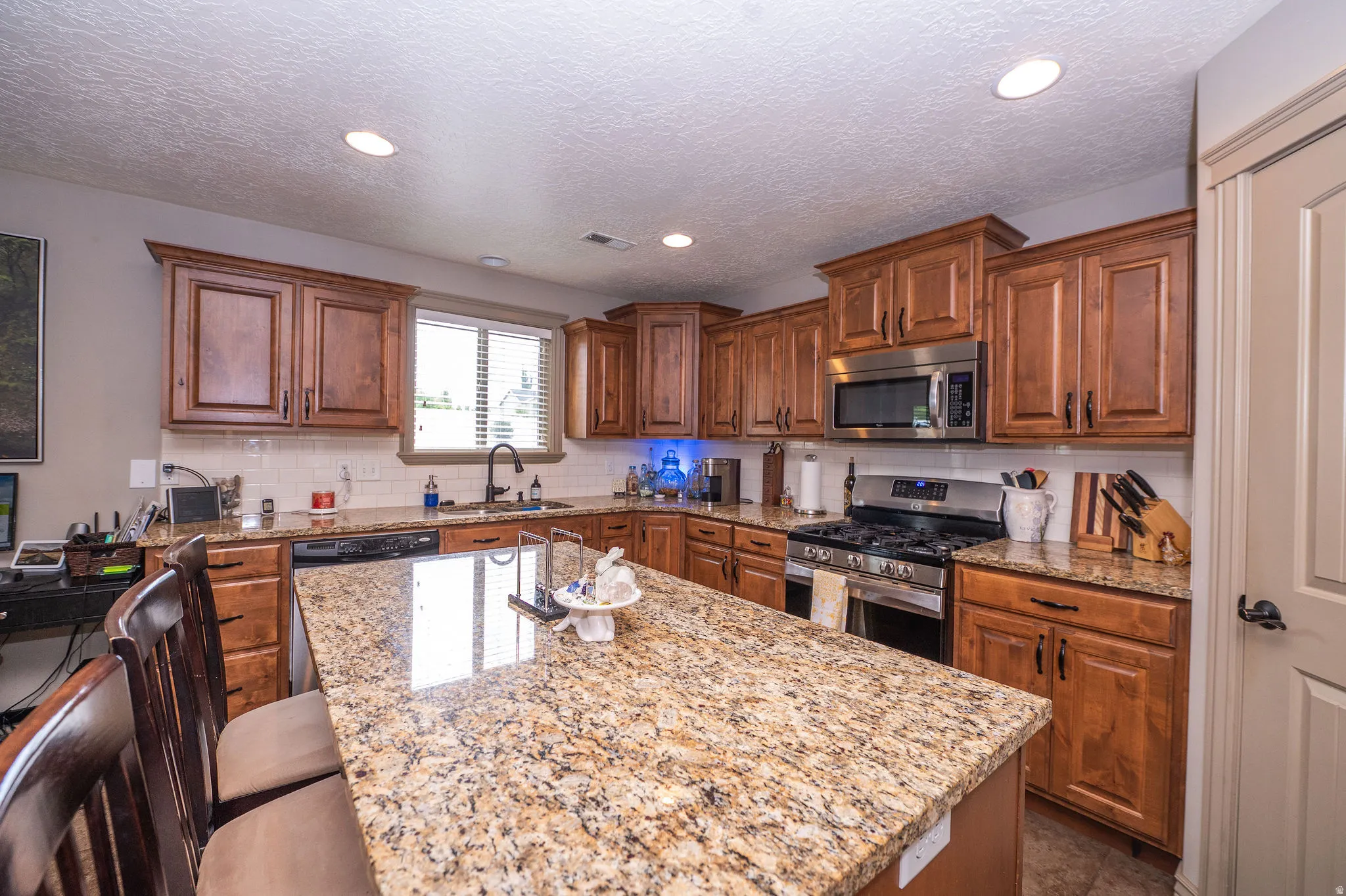 Kitchen featuring a large central island with seating, extensive wood cabinetry, granite countertops, and stainless steel appliances