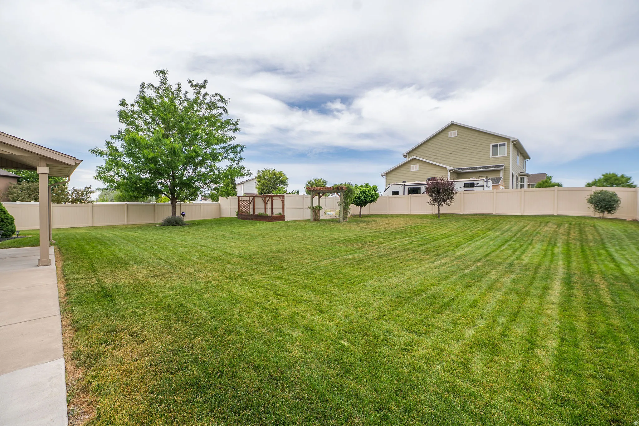 Expansive green lawn framed by a privacy fence, featuring a paved patio area, mature trees, and a wooden deck structure