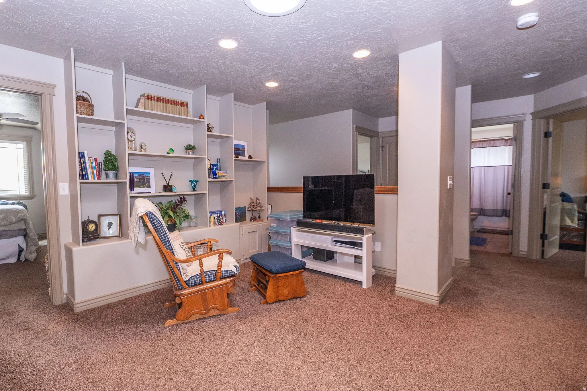 Carpeted recreation room featuring extensive built-in shelving, recessed ceiling lighting, and multiple doorways leading to additional interior spaces