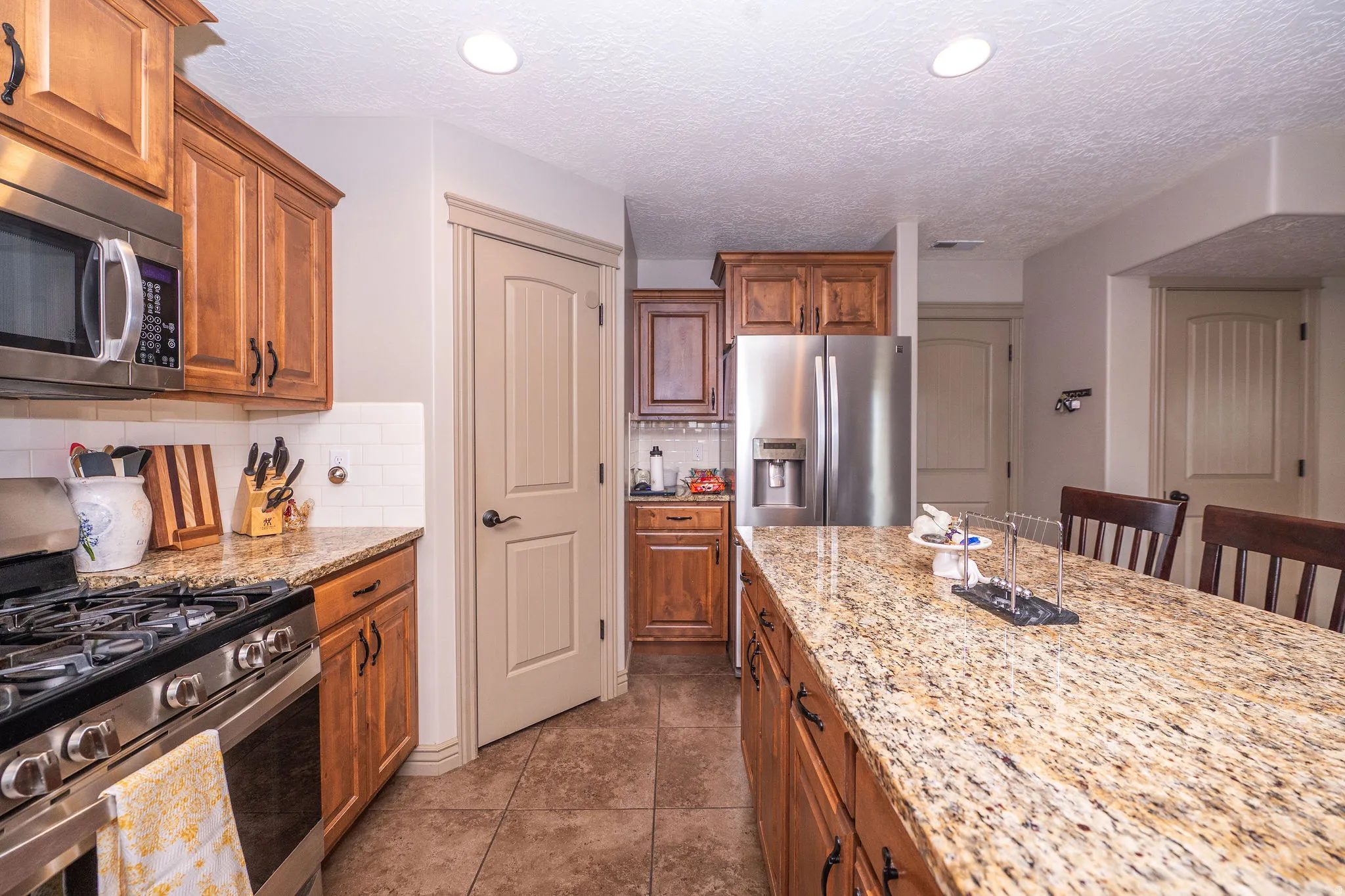 Kitchen featuring wood cabinetry, granite countertops, stainless steel appliances, a tile backsplash, and tile flooring
