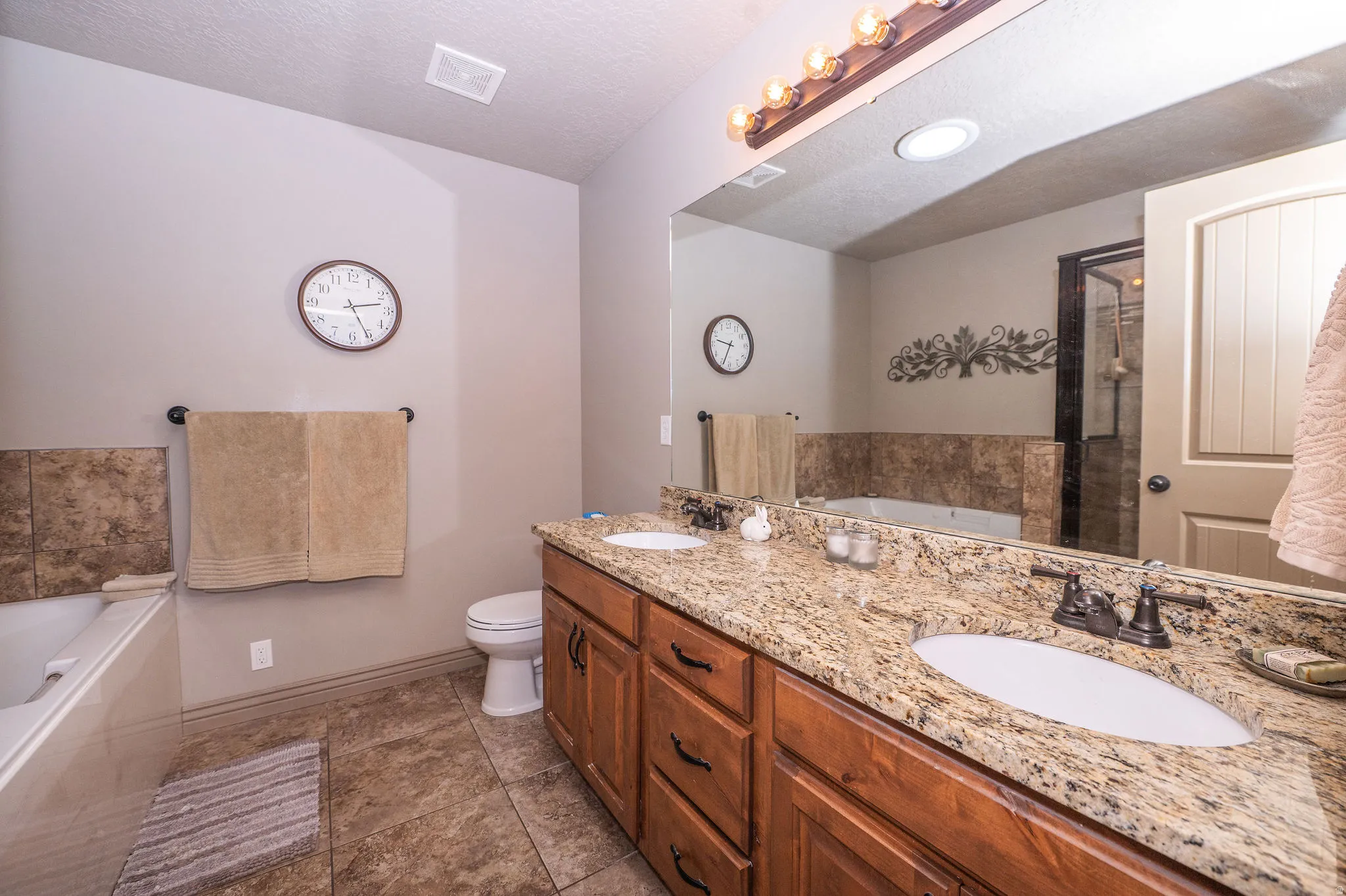 Bathroom featuring a dual vanity with granite countertops, wood cabinetry, and a large mirror