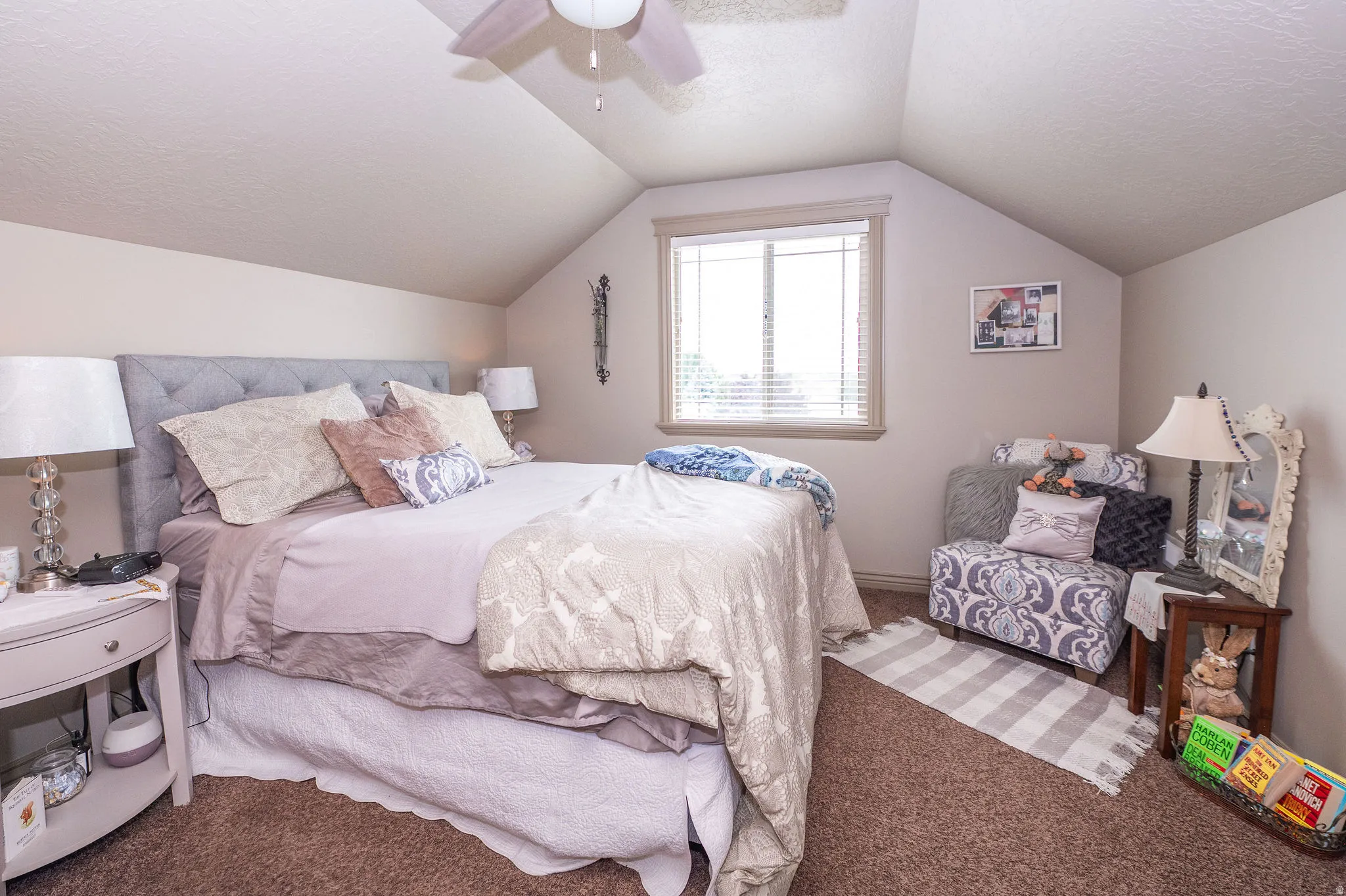 Carpeted room featuring a tufted fabric headboard, a window with horizontal blinds, sloped ceilings, and a ceiling fan