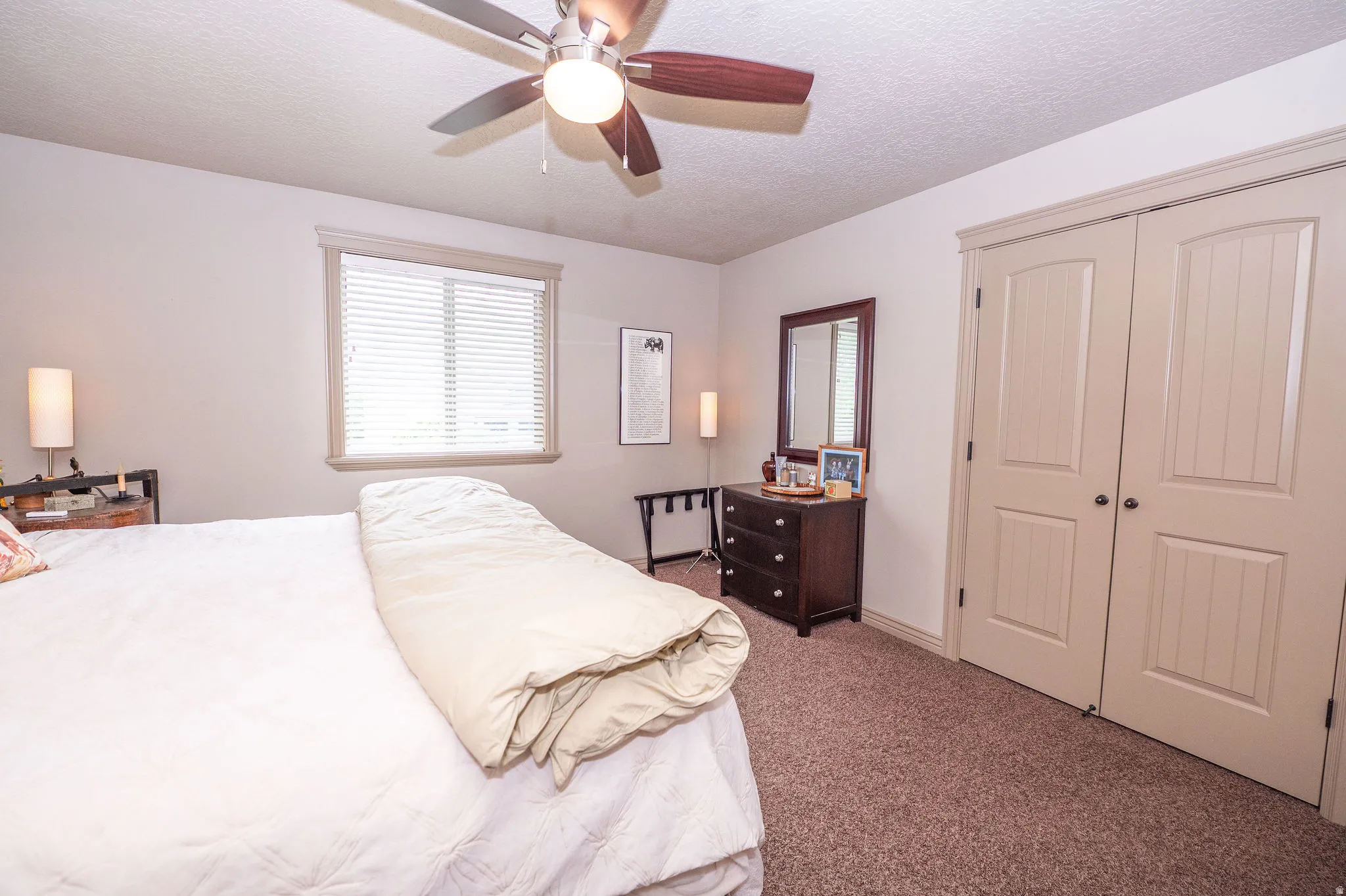 Carpeted room featuring a ceiling fan with integrated lighting, a window with blinds, and two panel-style closet doors