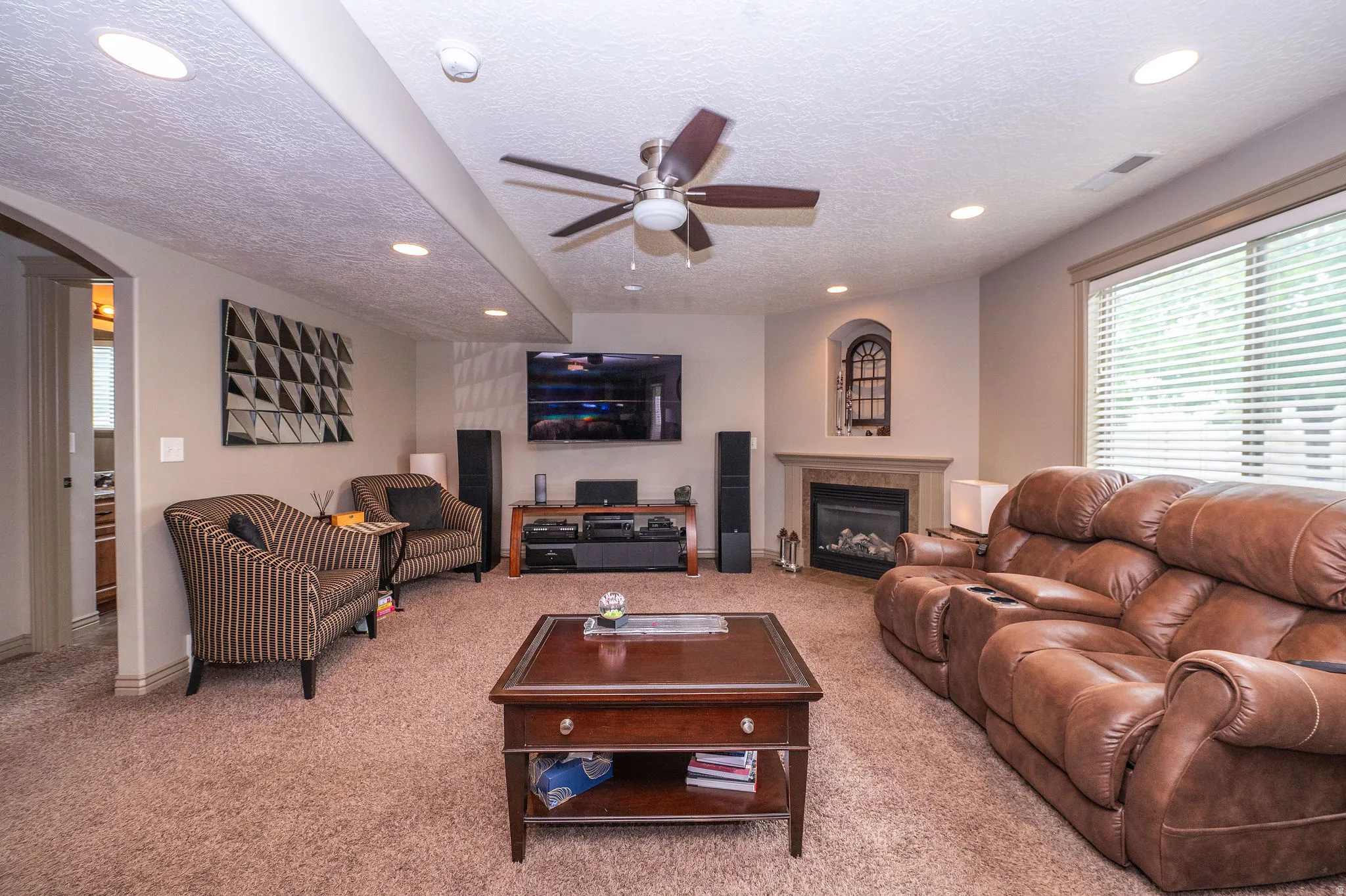 Spacious carpeted living area featuring a built-in electric fireplace with a stone surround, recessed lighting, and a ceiling fan