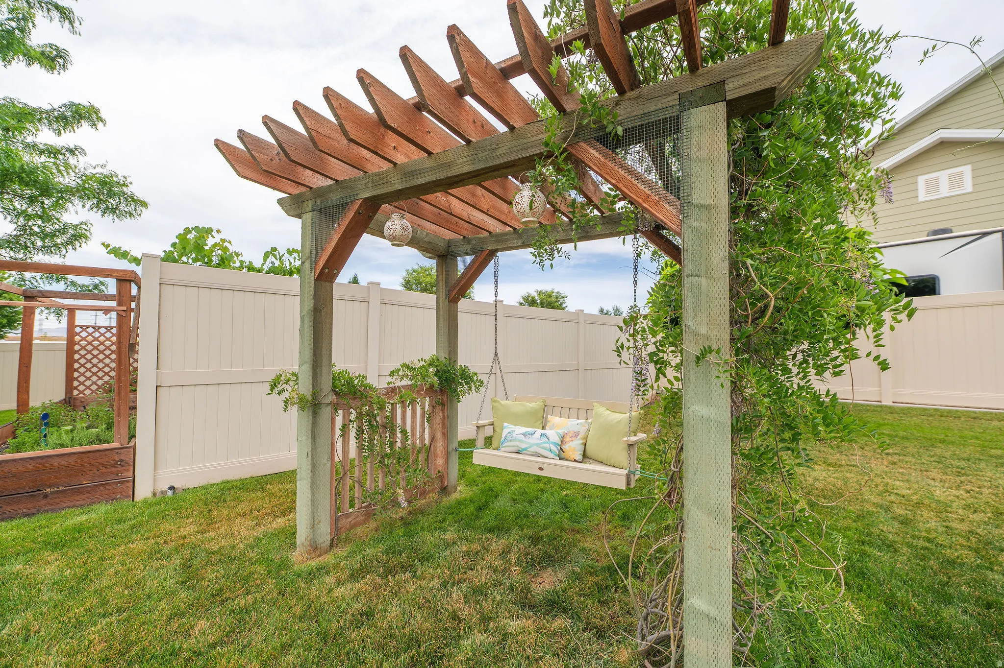 Backyard featuring a wooden pergola with climbing vines, a swing, and a raised garden bed with lattice detailing