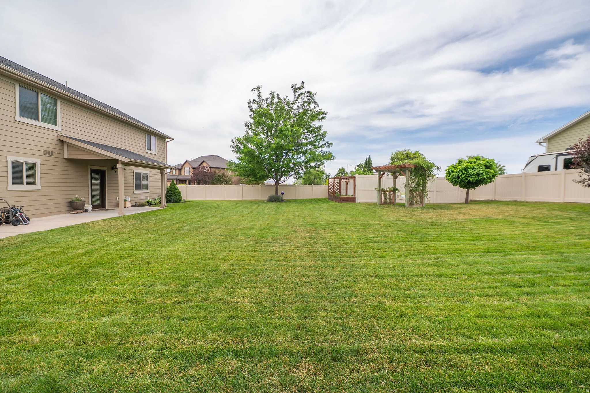Expansive backyard featuring a manicured lawn, established trees, and a wooden pergola structure