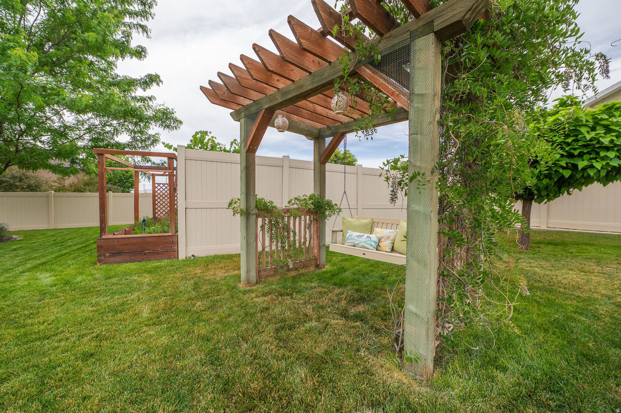 Expansive green lawn featuring a wooden pergola with a built-in porch swing, adorned with climbing vines