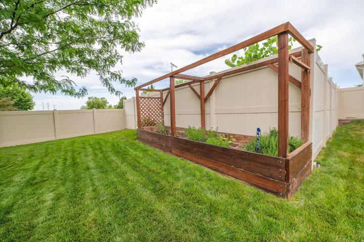 Expansive backyard featuring a manicured lawn and a substantial raised garden bed with an integrated wood-frame trellis