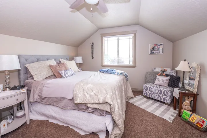 Carpeted room featuring a tufted fabric headboard, a window with horizontal blinds, sloped ceilings, and a ceiling fan
